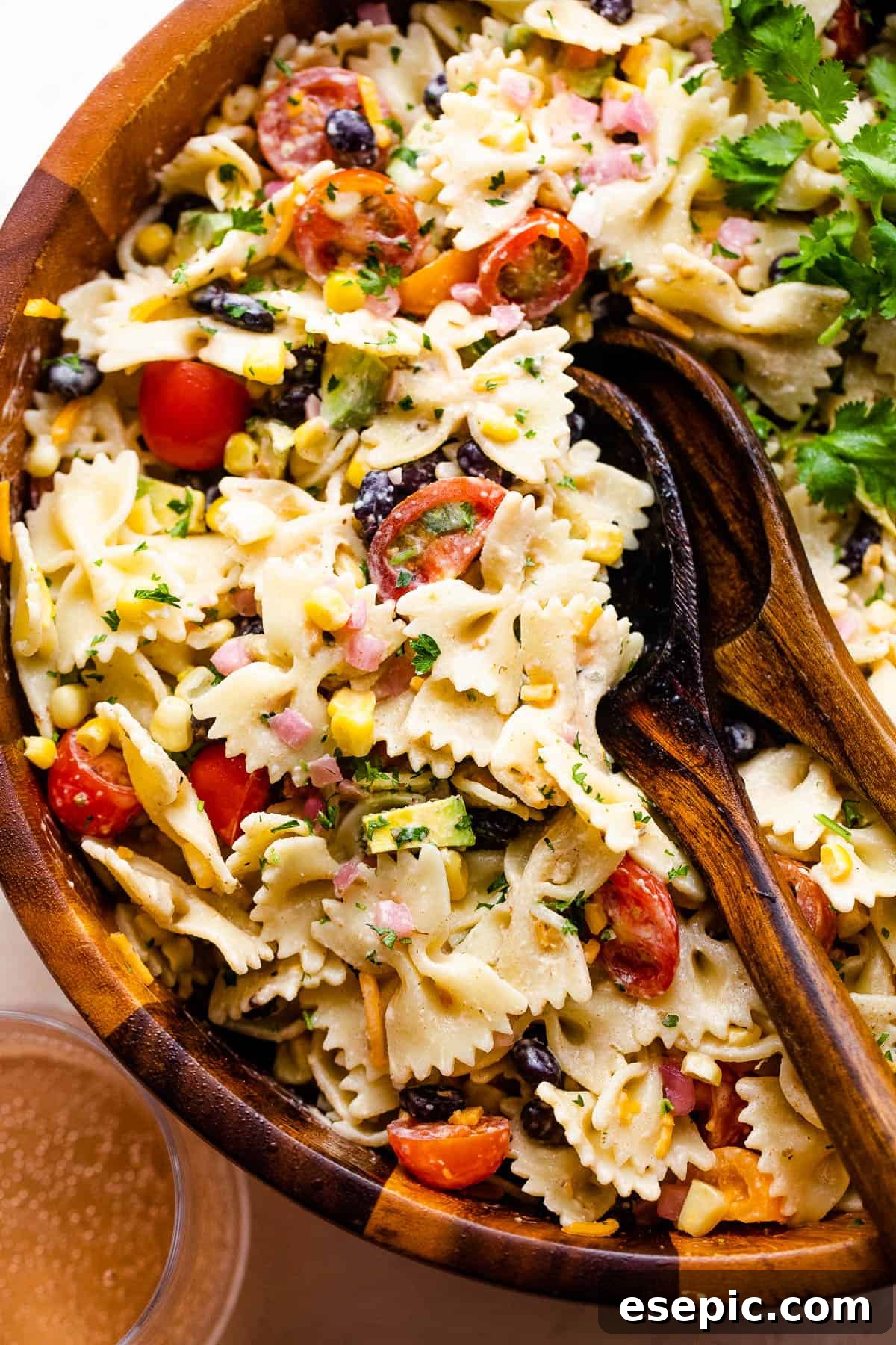 The finished Fiesta Pasta Salad displayed in a wooden salad bowl with two wooden serving spoons, ready for serving.