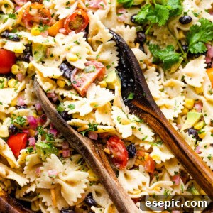 pasta salad in a wooden salad bowl with two wooden spoons