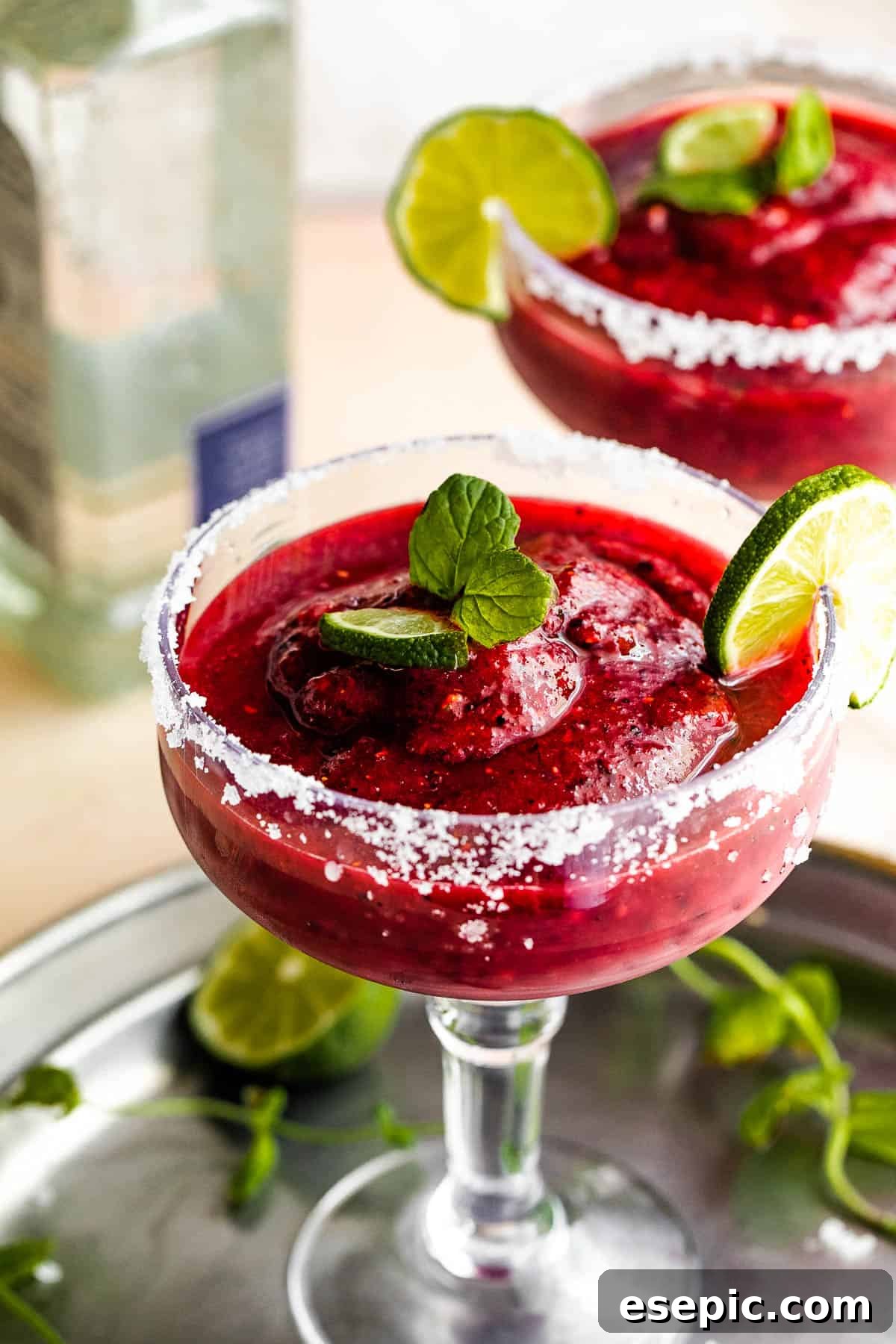 Frozen Berry Margarita served in a margarita glass with salted rims, slice of lime, and mint