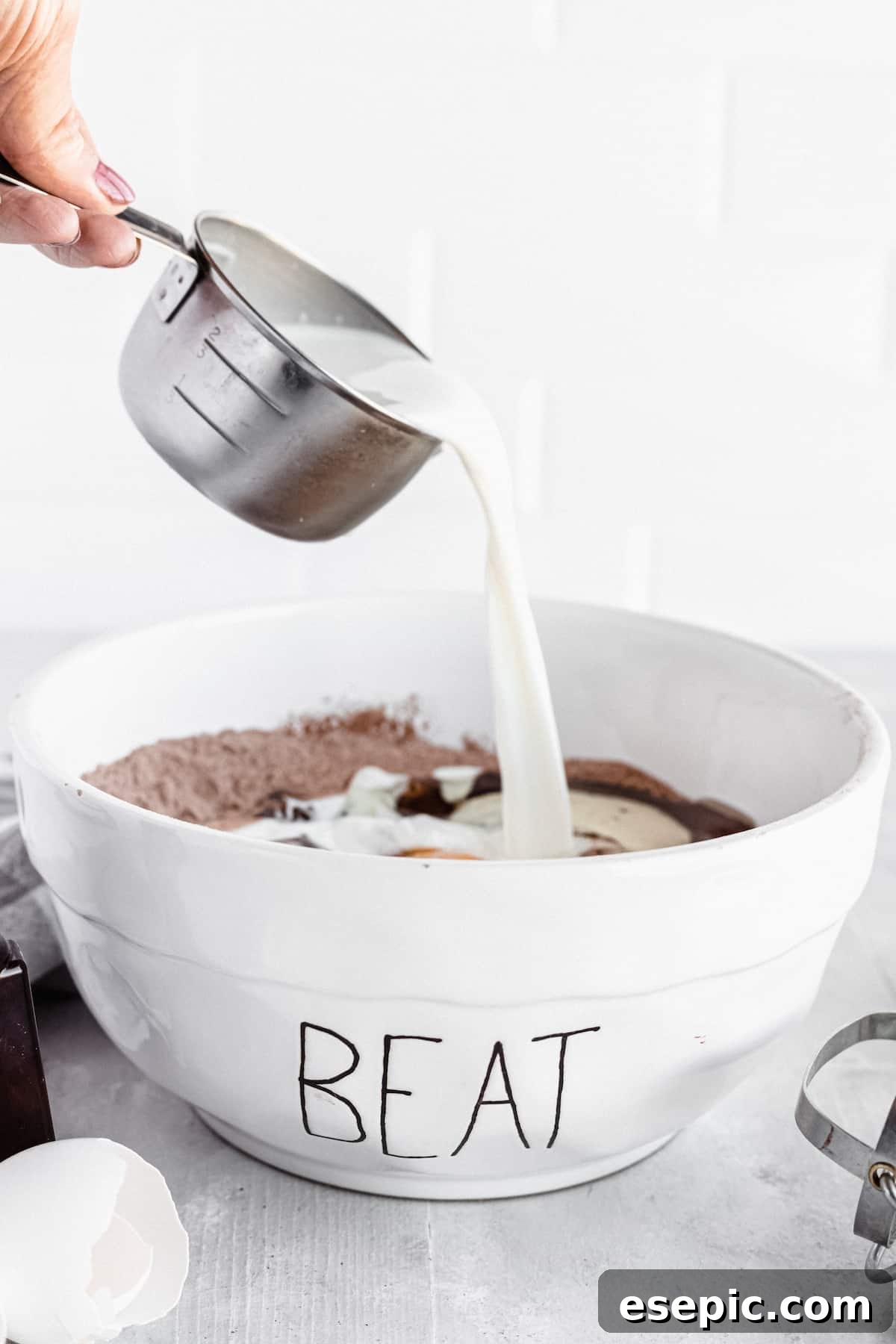 Whole milk being carefully poured into a mixing bowl containing the ingredients for a homemade chocolate cake.