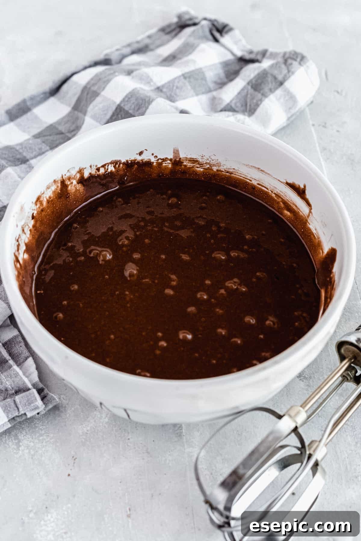 A white mixing bowl brimming with smooth, dark chocolate cake batter, awaiting transfer to the baking pans.