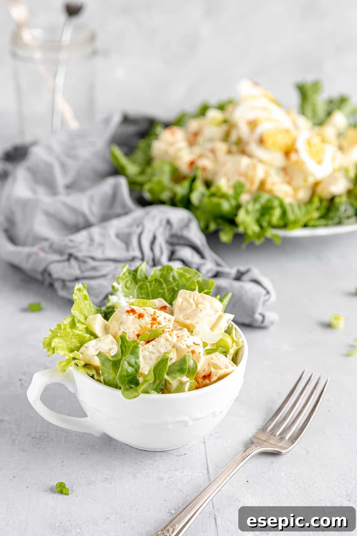 A Single Serving of American Classic Potato Salad in a Rustic Mug, with a Larger Bowl of Salad in the Soft-Focus Background