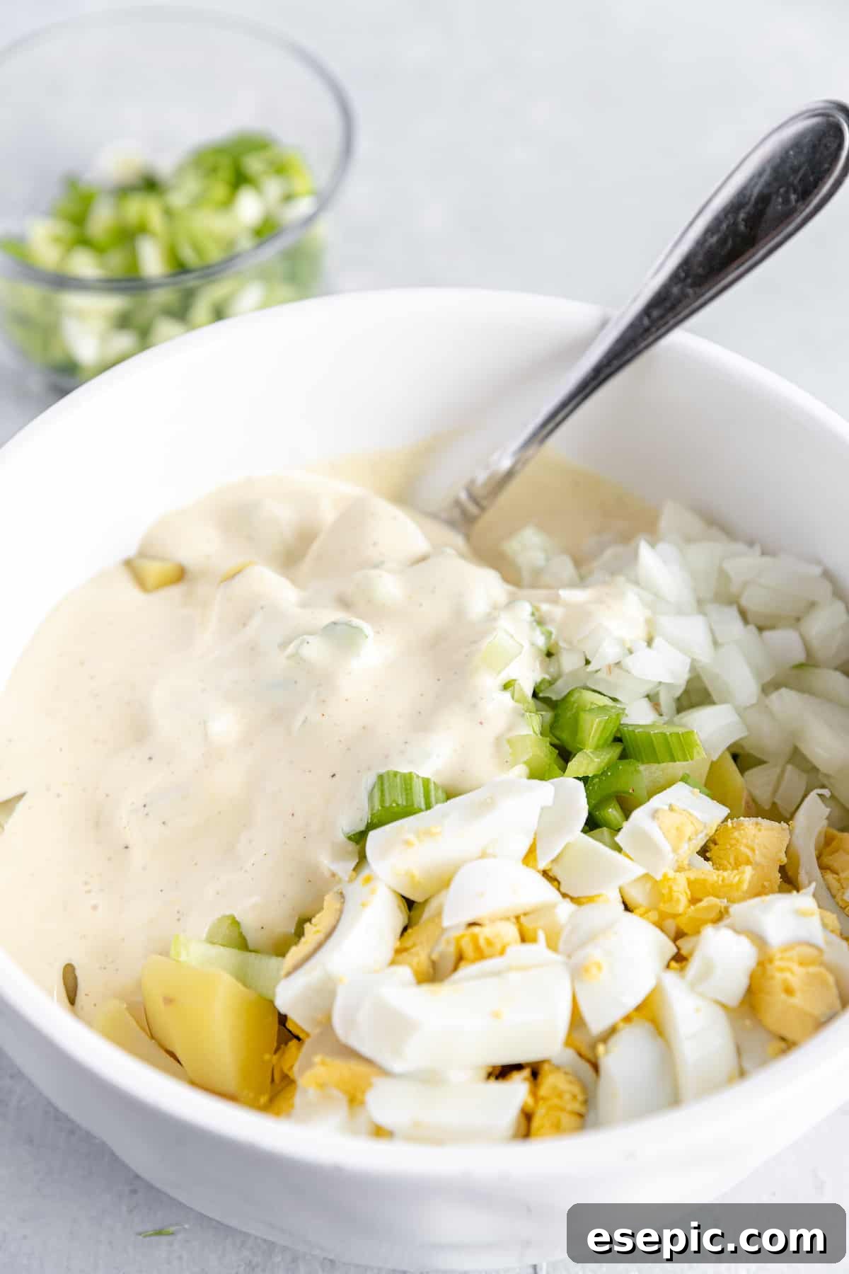 Creamy Mayonnaise Dressing Being Poured into a Bowl of Unmixed Potato Salad Ingredients