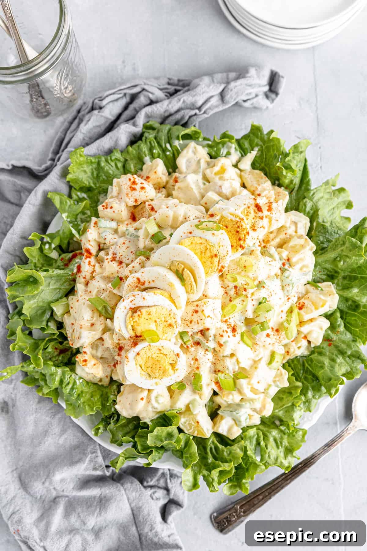 An Overhead Shot of American Classic Potato Salad on a Lettuce-Lined Plate, Resting Beside a Textured Gray Kitchen Towel