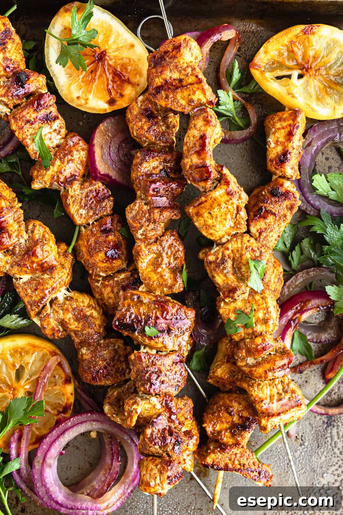 Five Shawarma Grilled Chicken Skewers on a Metal Pan with Onions, Lemon Slices and More