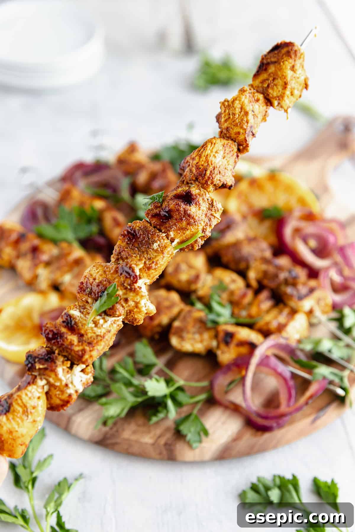 A Shawarma Grilled Chicken Skewer Being Held Above a Platter Containing More Kebabs