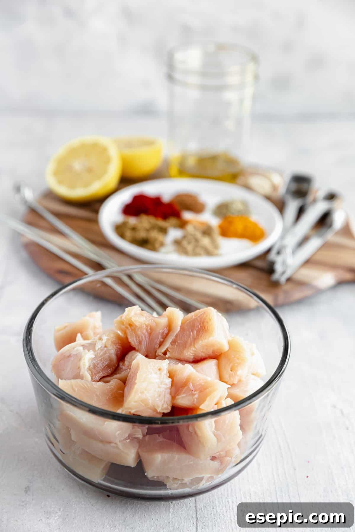 Cubes of Boneless, Skinless Chicken Breast with Spices and the Remaining Kebab Ingredients in the Background