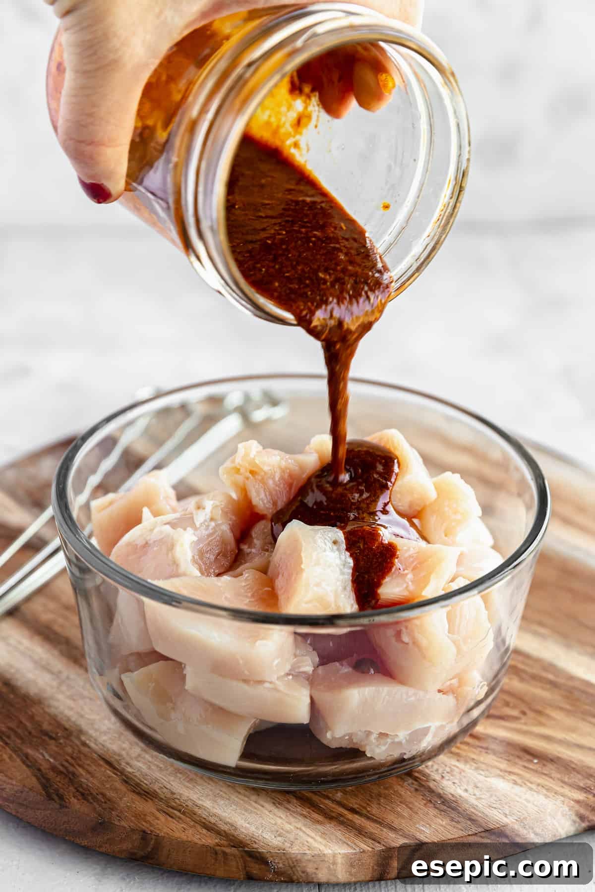 A Dish of Raw, Cubed Chicken Breast with a Jar of Shawarma Marinade Being Poured Into it