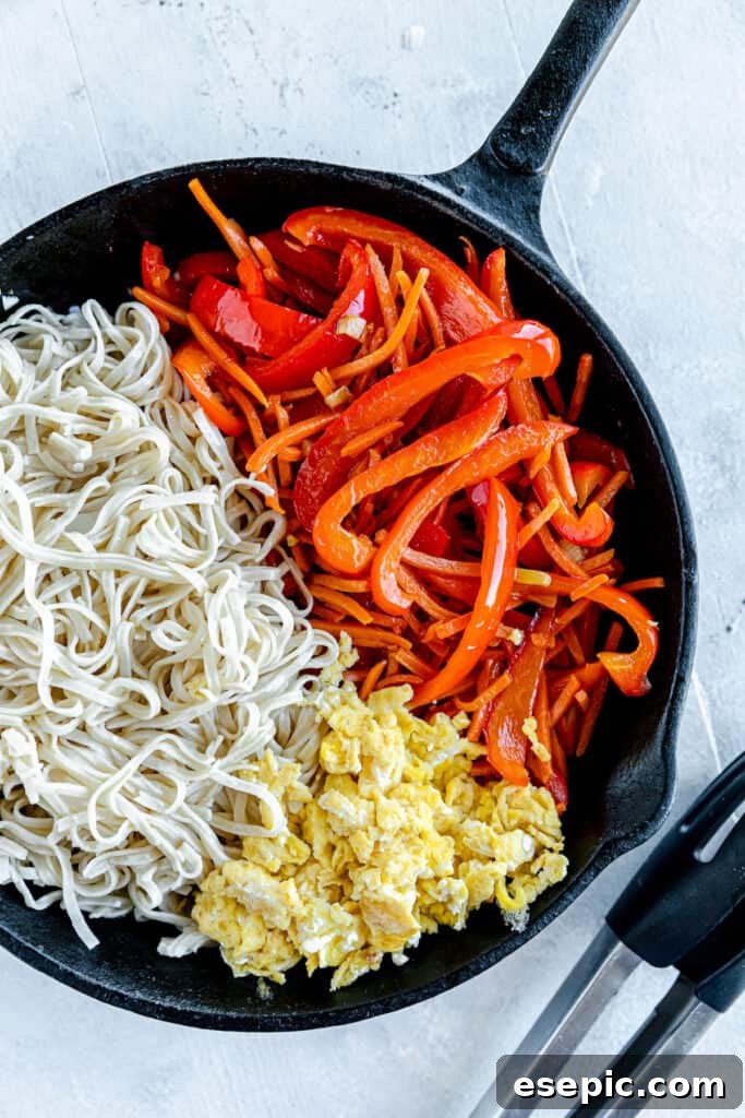 Scrambled Eggs, Brown Rice Noodles and Chopped Veggies Inside of a Black Skillet, beautifully mixed.