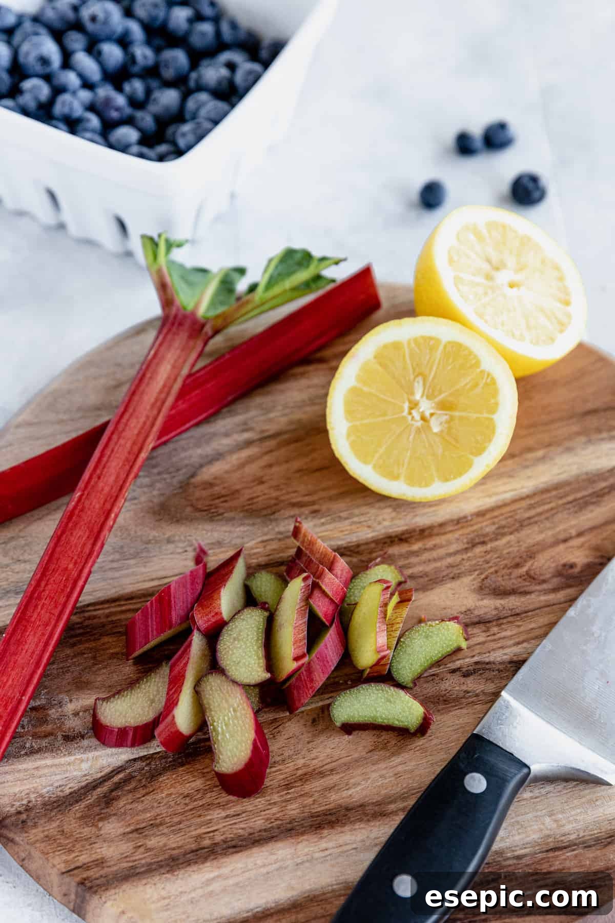 Chopped Rhubarb and a Halved Lemon on a Cutting Board with a Bowl of Blueberries in the Background, showing fresh ingredients