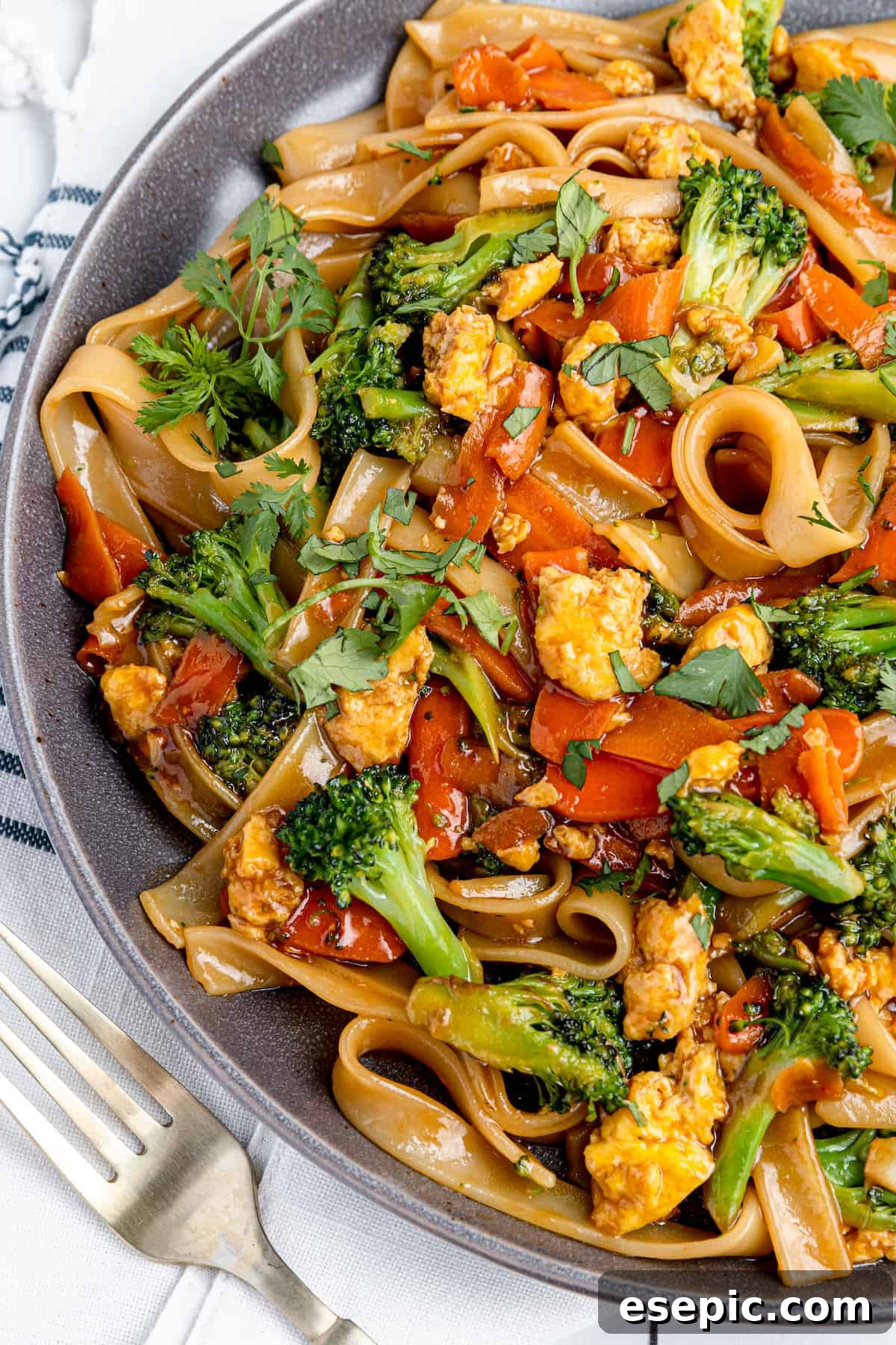 A Large Plate Filled with Pad See Ew Beside a Metal Fork, showcasing the rich brown noodles and green broccoli.