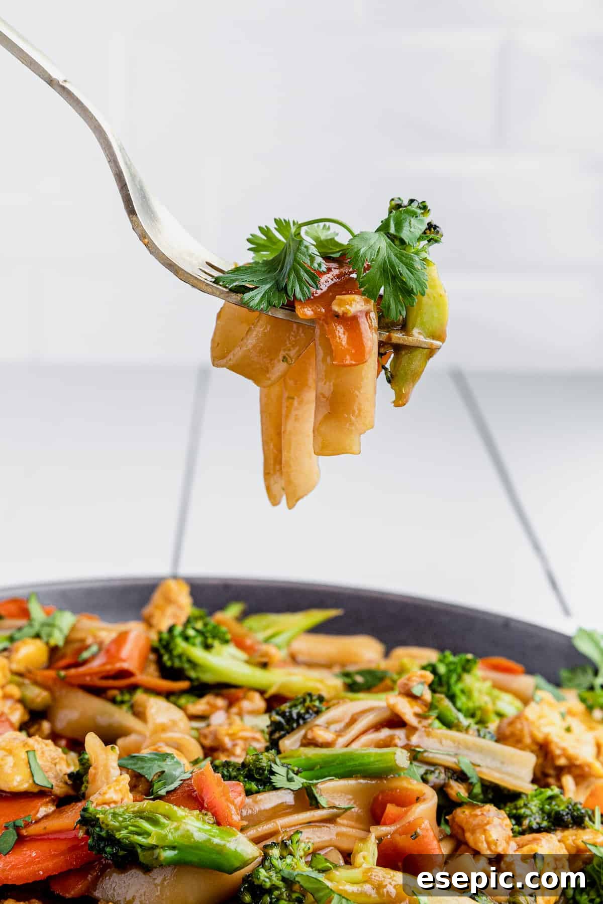 A close-up shot of a fork lifting a bite of Pad See Ew, showing the noodles, egg, and broccoli in detail.