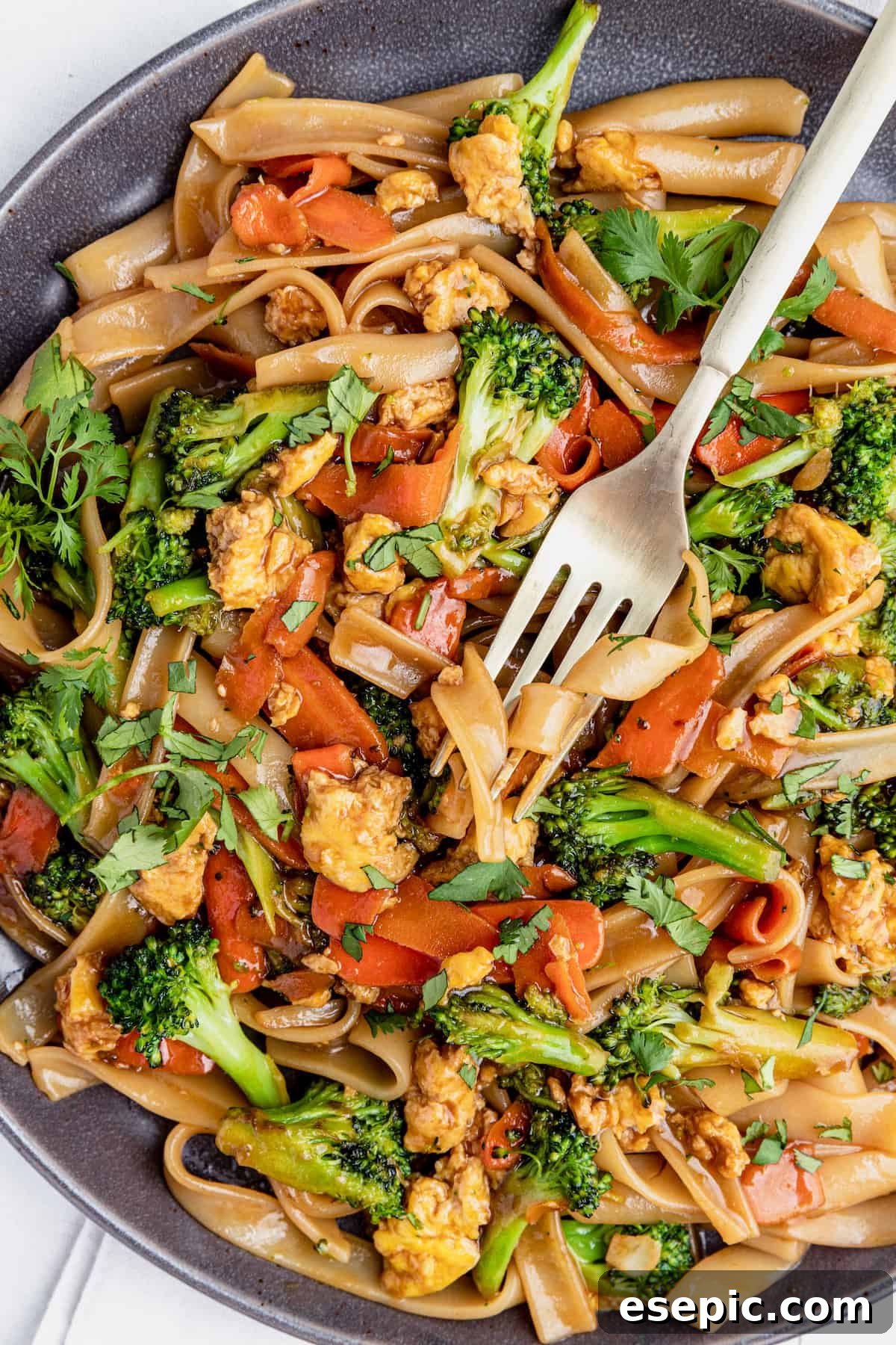 A fork digging into a generous portion of freshly made Pad See Ew on a white plate, highlighting the steam and rich sauce.