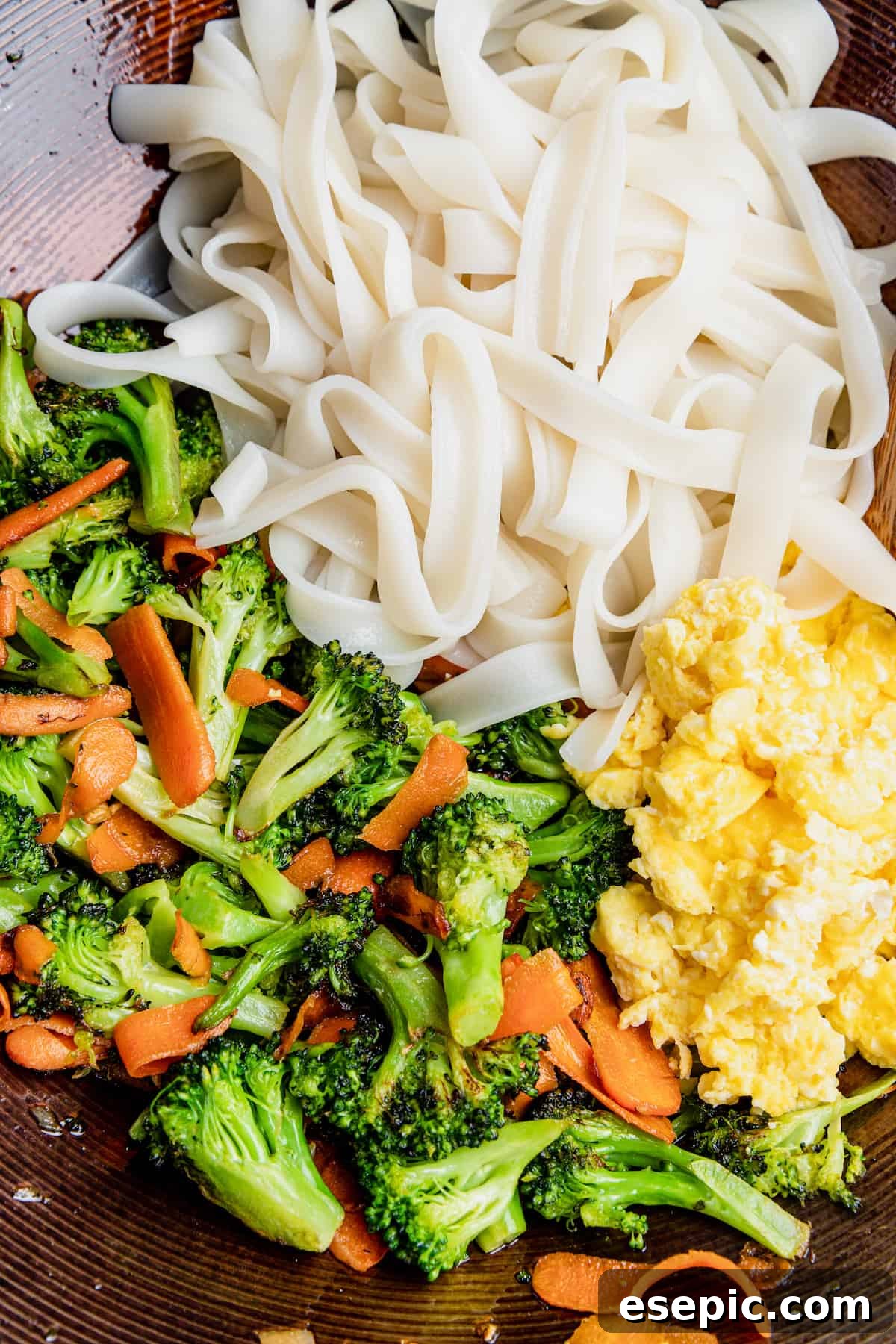 A bowl of perfectly cooked wide rice noodles, scrambled eggs, and tender vegetables, ready for the sauce.