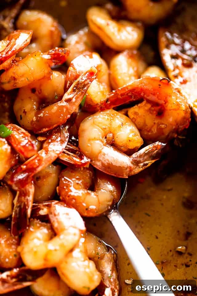 Honey Garlic Shrimp: A quick, easy, and incredibly flavorful shrimp recipe cooked in one skillet with just 5 ingredients in 20 min! A close-up of a spoon stirring cooked honey garlic shrimp in a skillet, highlighting the glossy sauce and perfectly cooked pink shrimp.