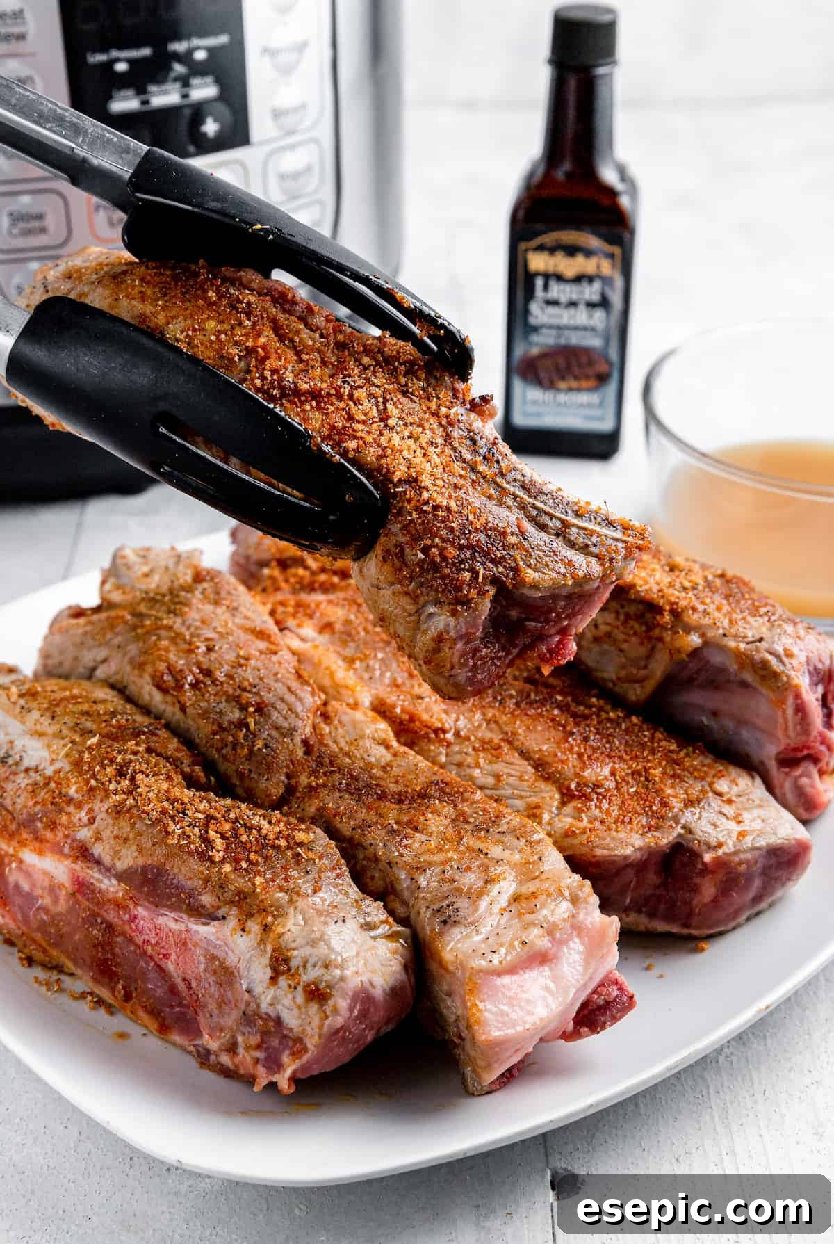 A Pair of Tongs Holding a Seasoned Pork Rib Over a Plate Full