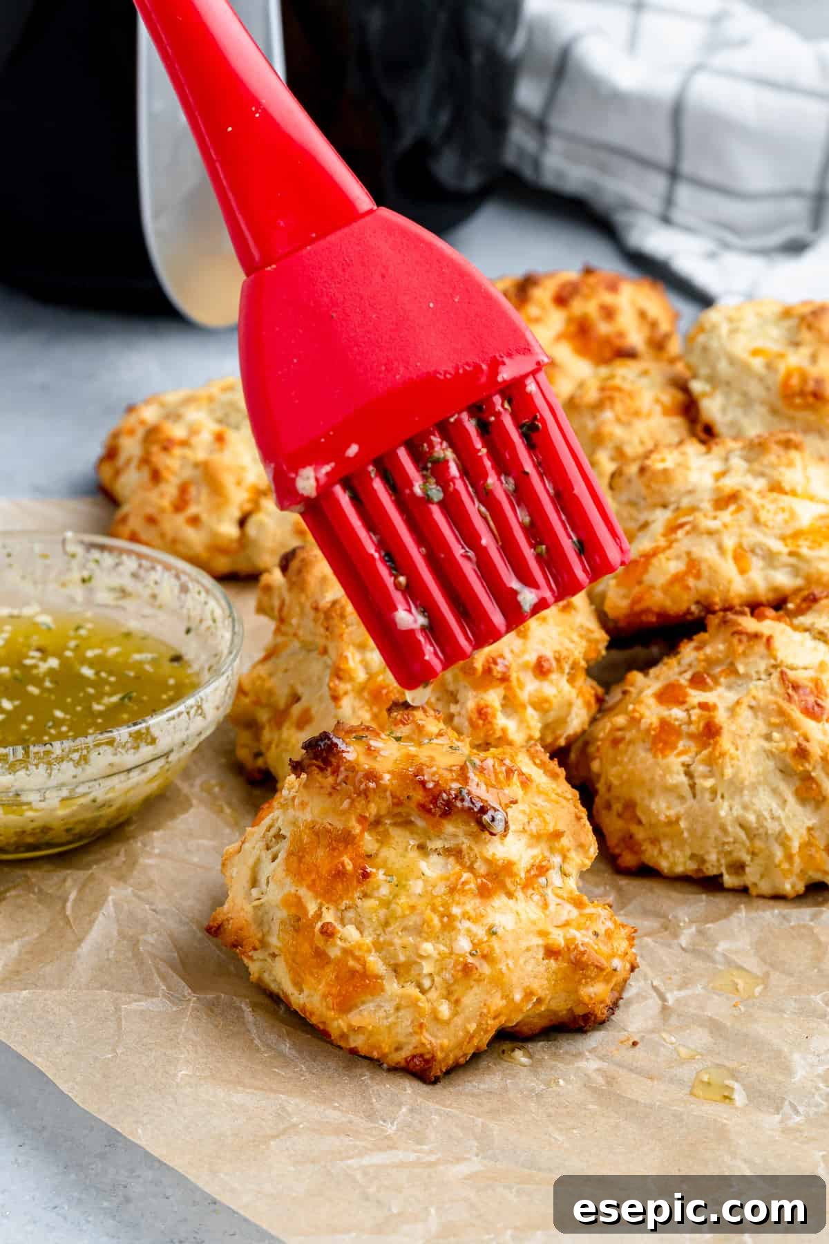 A hand using a red pastry brush to glaze a warm, golden Air Fryer Red Lobster Biscuit with savory garlic butter.