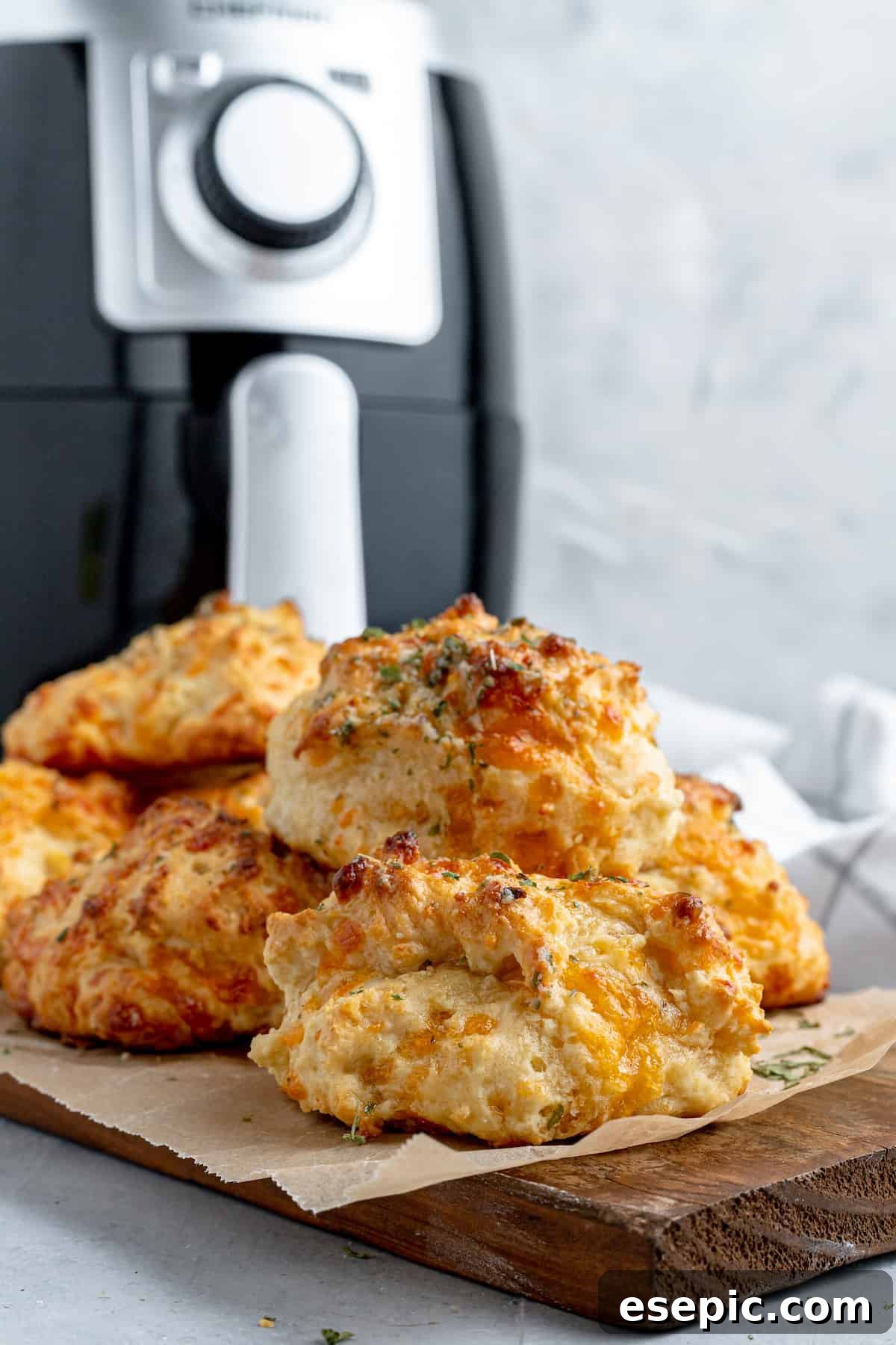 A rustic cutting board laden with a generous pile of golden Air Fryer Red Lobster Biscuits, with an air fryer subtly blurred in the background.