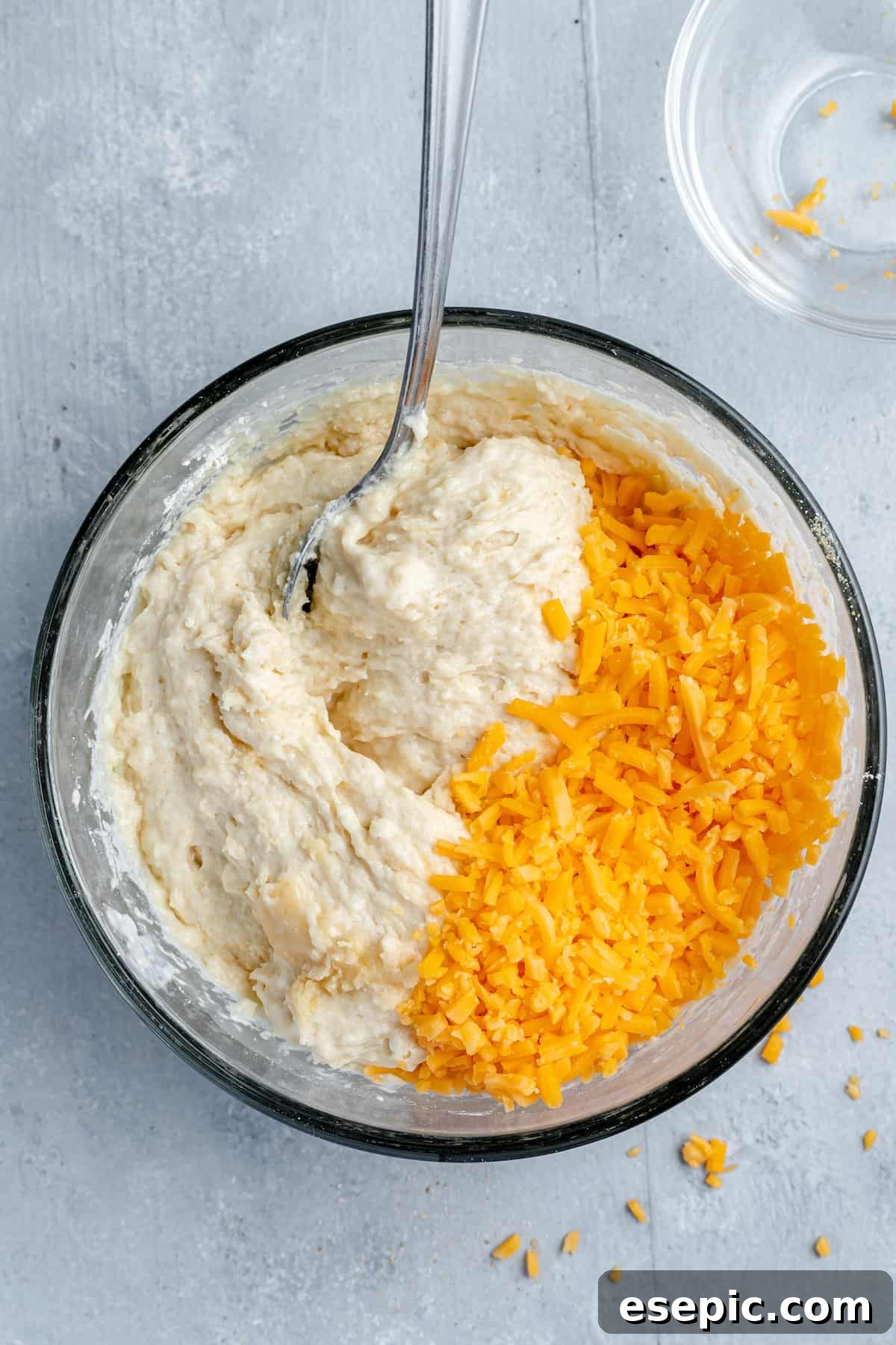 Shredded cheddar cheese being gently folded into the biscuit batter with a spoon to ensure even distribution.