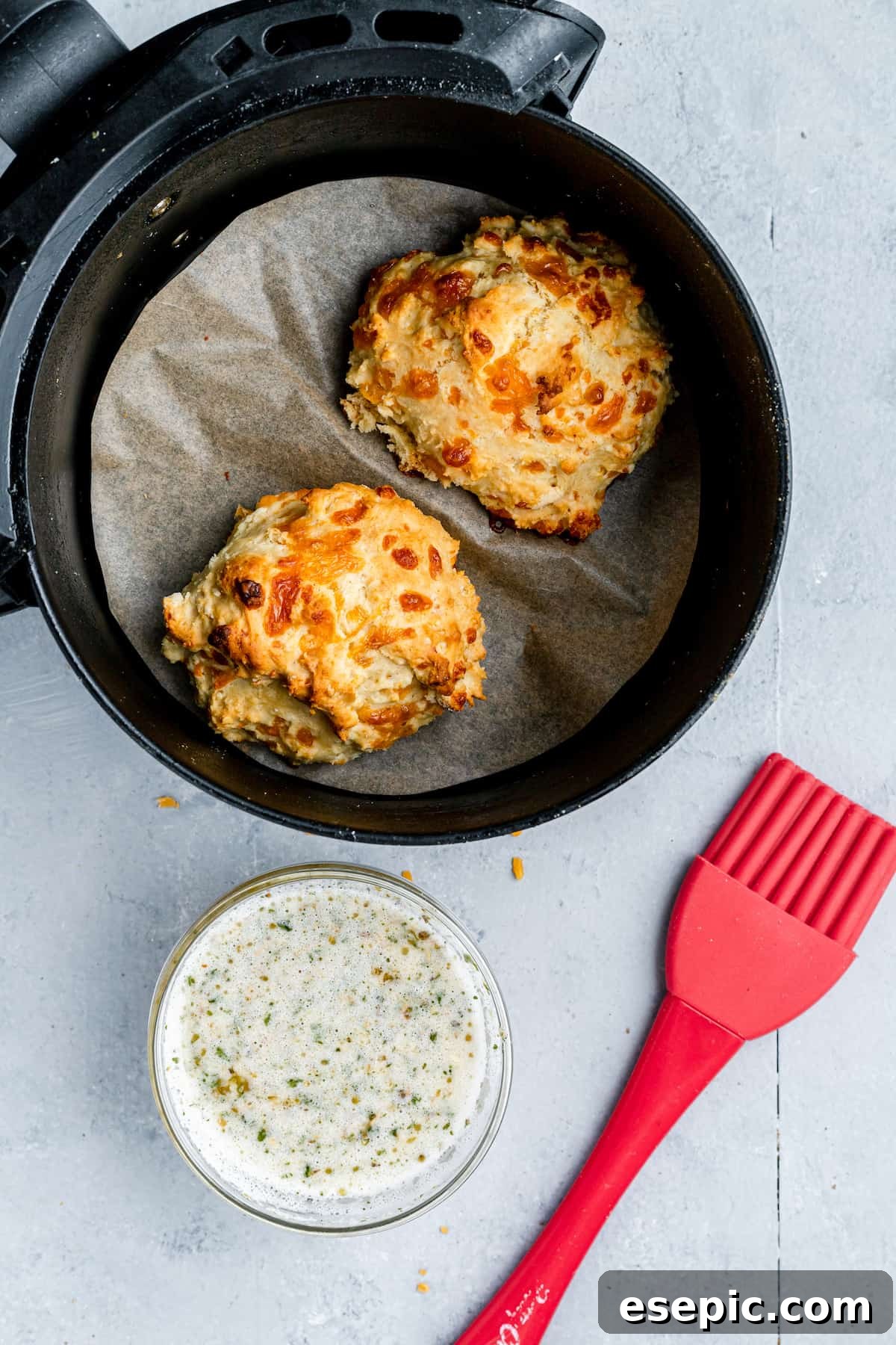 Two golden-brown Air Fryer Red Lobster Biscuits resting in the air fryer basket next to a small dish of fragrant garlic butter.