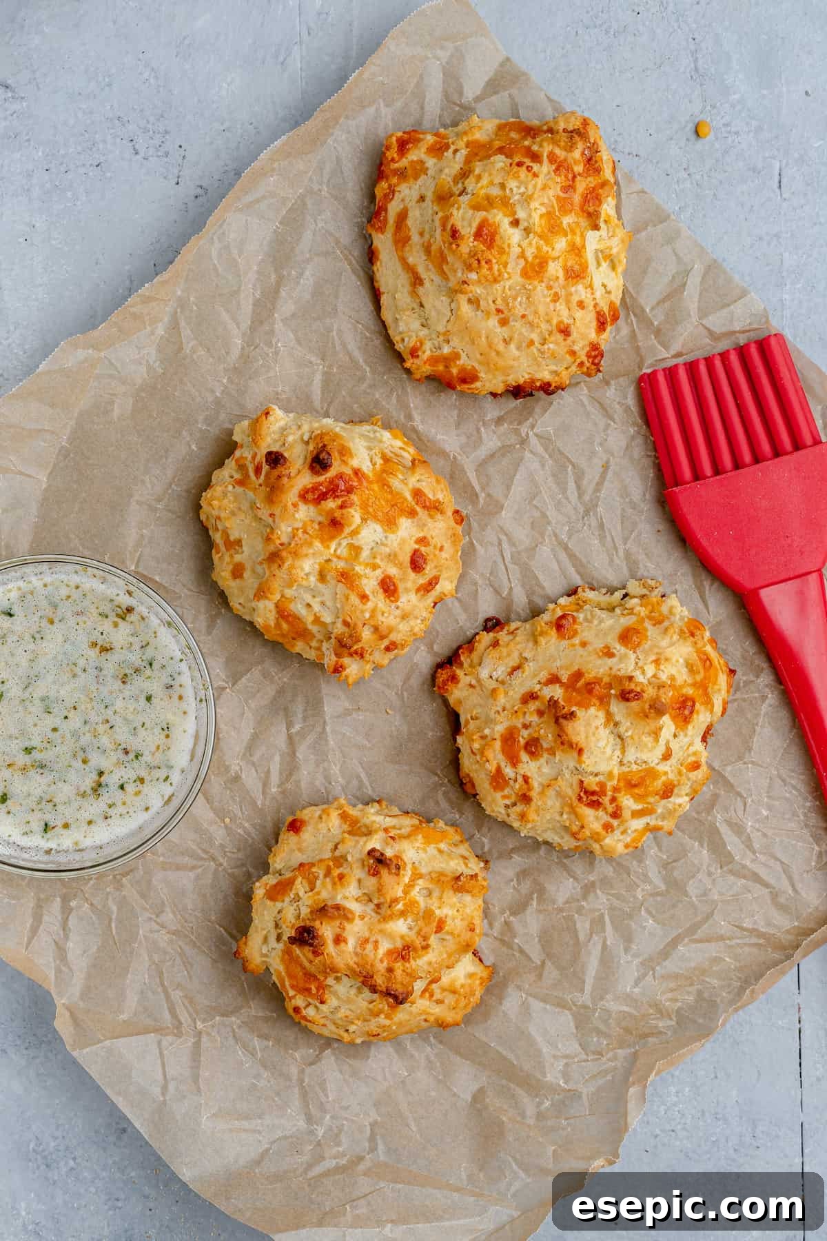 Four air-fried biscuits on a piece of parchment paper, accompanied by a pastry brush and a small dish of garlic butter for glazing.