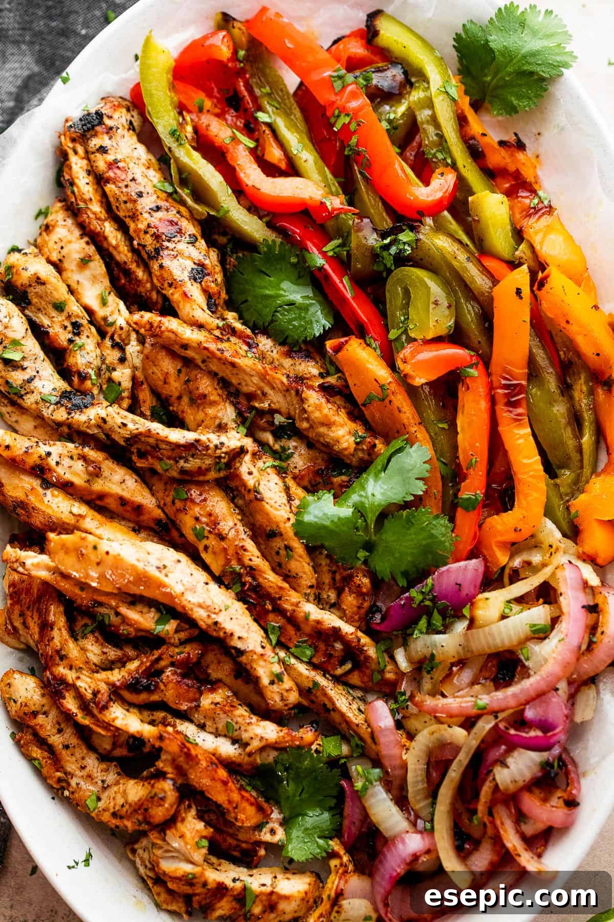 Easy grilled chicken fajitas featuring juicy chicken, onions, and peppers, served in warm tortillas with your favorite toppings. grilled chicken strips, colorful bell pepper strips, and onions on a serving plate garnished with cilantro leaves