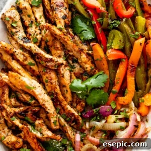 grilled chicken fajitas with chicken strips, colorful bell pepper strips, and onions on a serving plate garnished with cilantro leaves