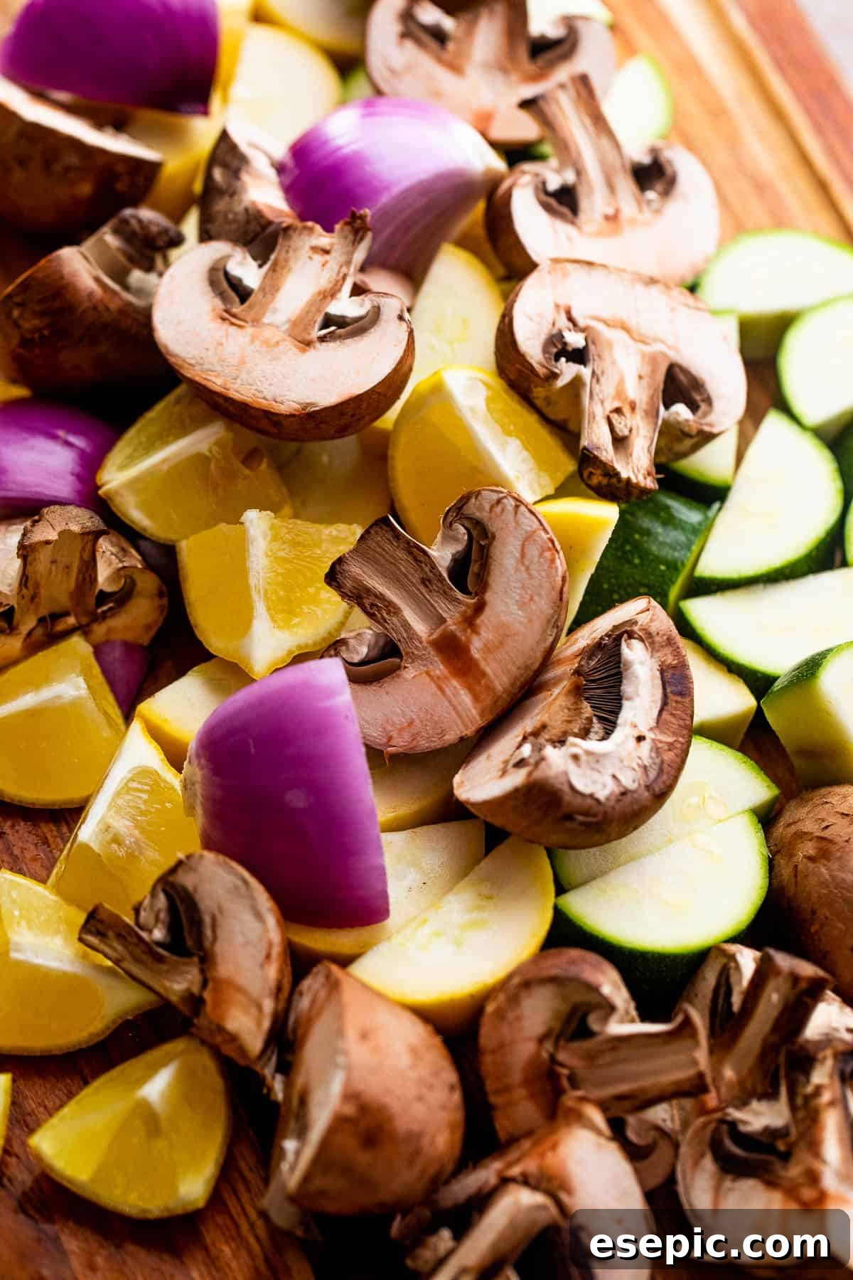 A colorful array of chopped mushrooms, red onions, lemons, zucchini, and yellow squash neatly arranged on a rustic wooden board, ready for skewering.
