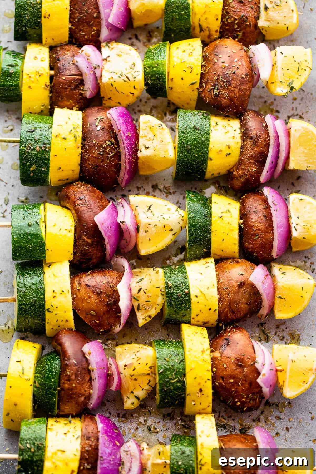 Eight perfectly grilled skewers featuring zucchini, yellow squash, red onions, mushrooms, and lemons arranged on a wooden serving board.