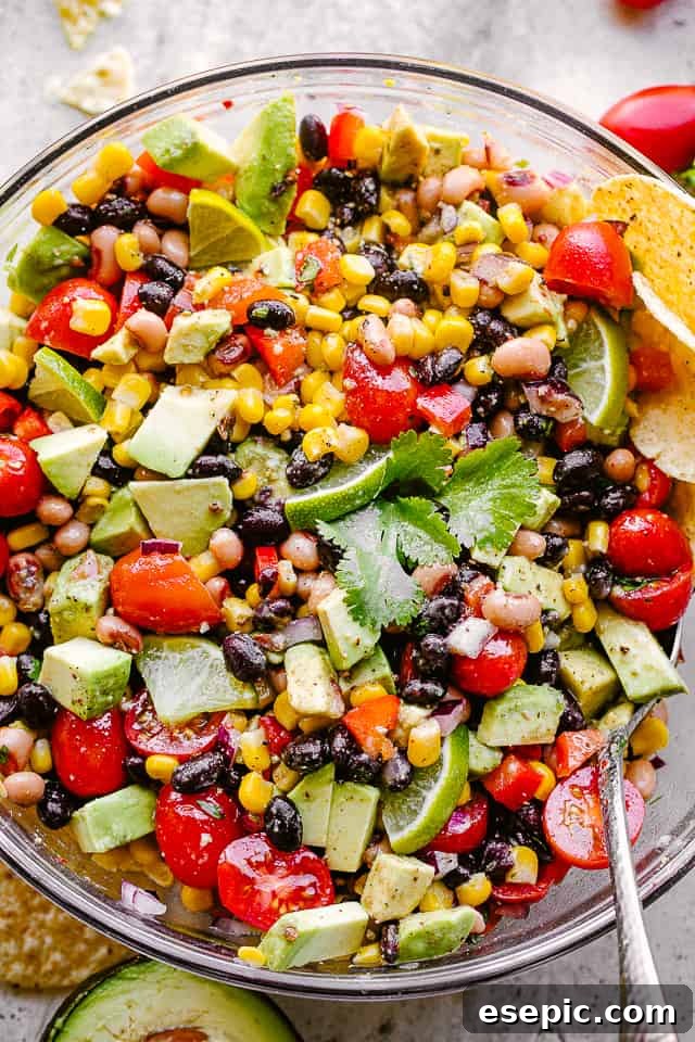 Close-up overhead shot of a colorful bowl of Cowboy Caviar, featuring corn, black beans, black-eyed peas, diced tomatoes, avocado, and cilantro.