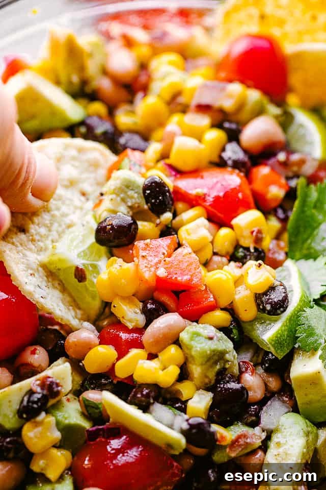 A tortilla chip scooping up a generous portion of colorful Cowboy Caviar from a glass bowl, showcasing the chunky texture.