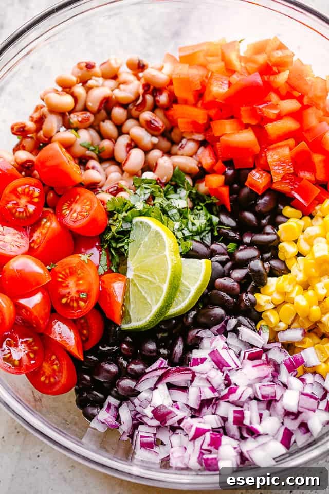 Avocado, corn, tomatoes, black-eyed peas, black beans, and cilantro arranged artfully in a large glass bowl before mixing, highlighting the individual fresh ingredients.