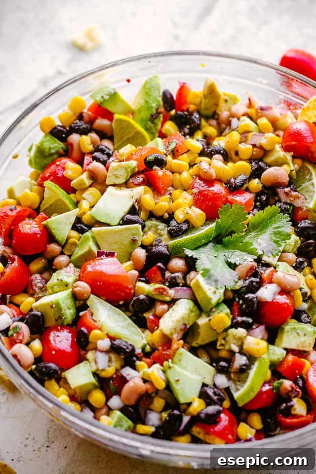 Avocado, corn, tomatoes, black-eyed peas, black beans, and cilantro in a large glass bowl, garnished and ready for serving, showcasing the vibrant colors.