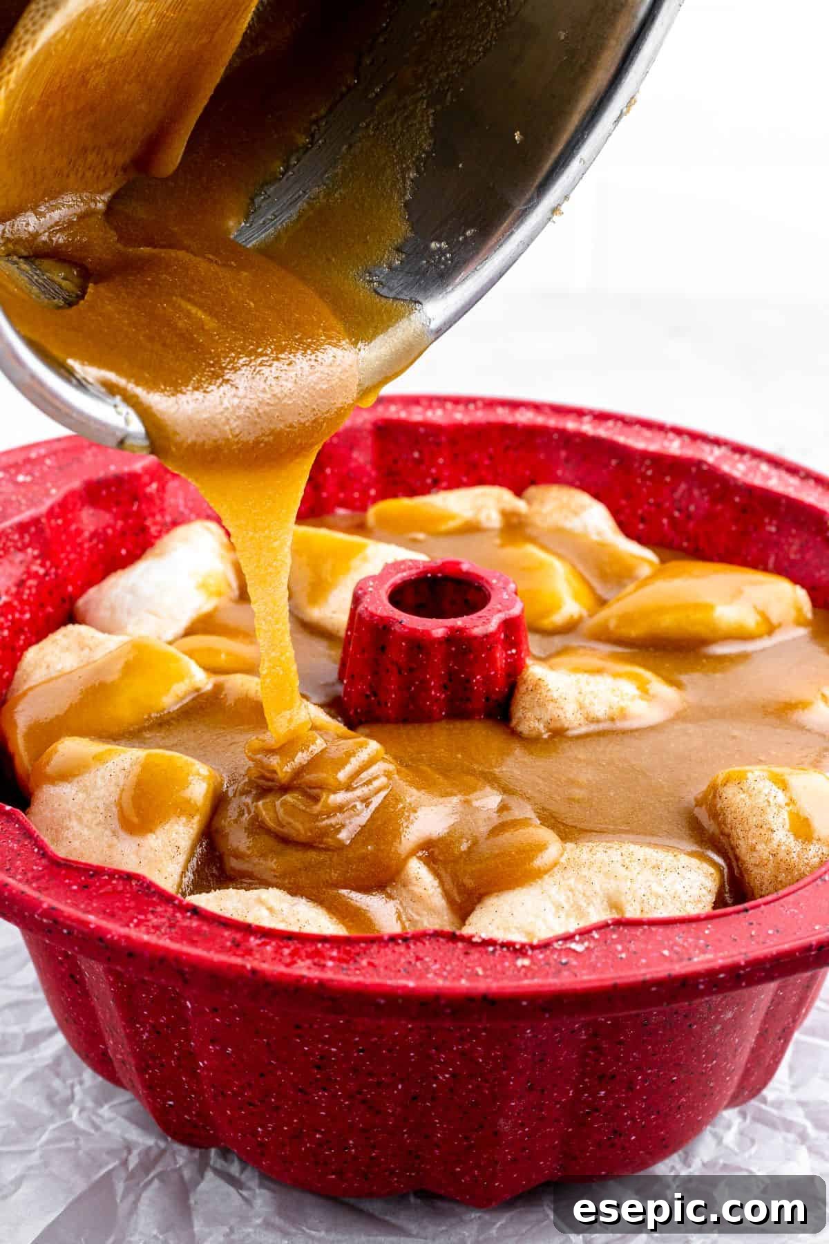 A thick brown-sugar-butter mixture is poured from a saucepan over biscuit dough pieces layered in a Bundt pan.