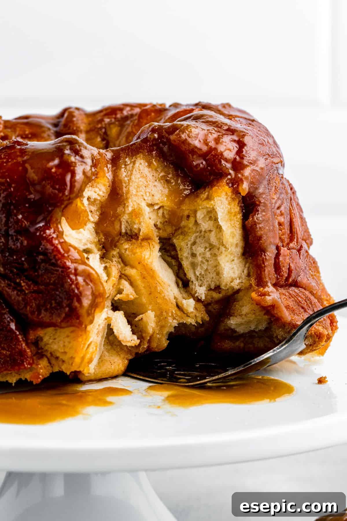 A baked monkey bread on a cake stand has several pieces removed, showcasing its pull-apart nature, with a cake server tucked underneath it.