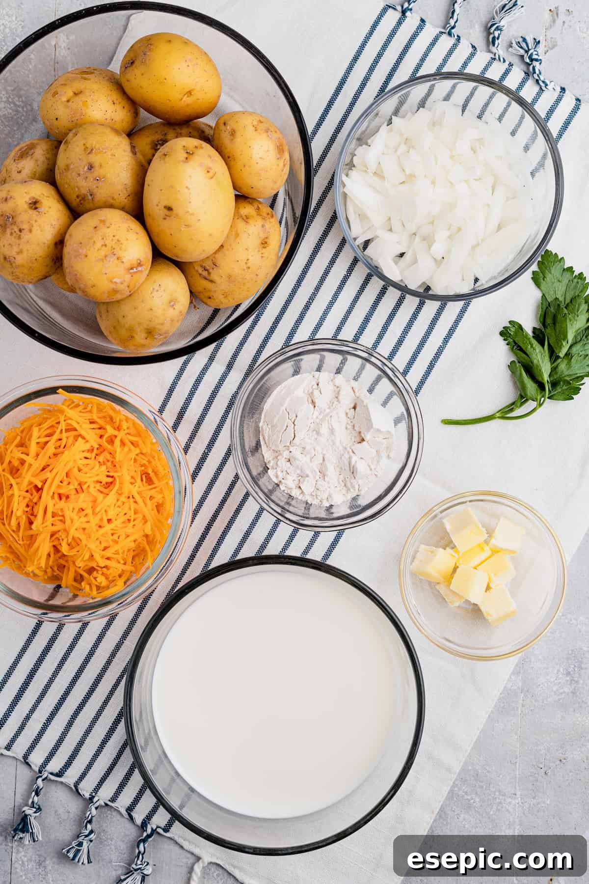Clockwise from top: finely diced onion, all-purpose flour, cubed butter, evaporated milk, shredded cheddar cheese, and whole washed Yukon Gold potatoes, ready for preparation.
