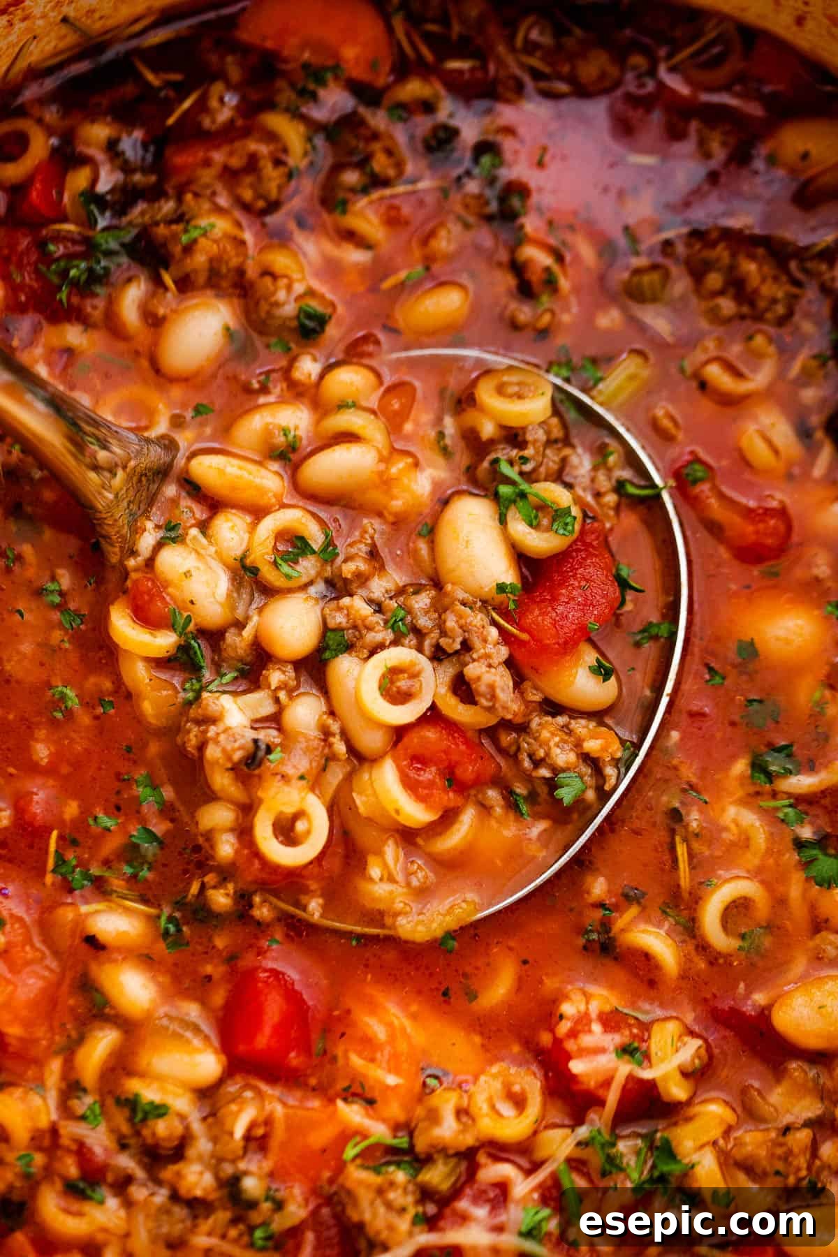 A close-up view of Pasta Fagioli soup being ladled from a pot, showcasing the rich texture of beans, pasta, and vegetables.