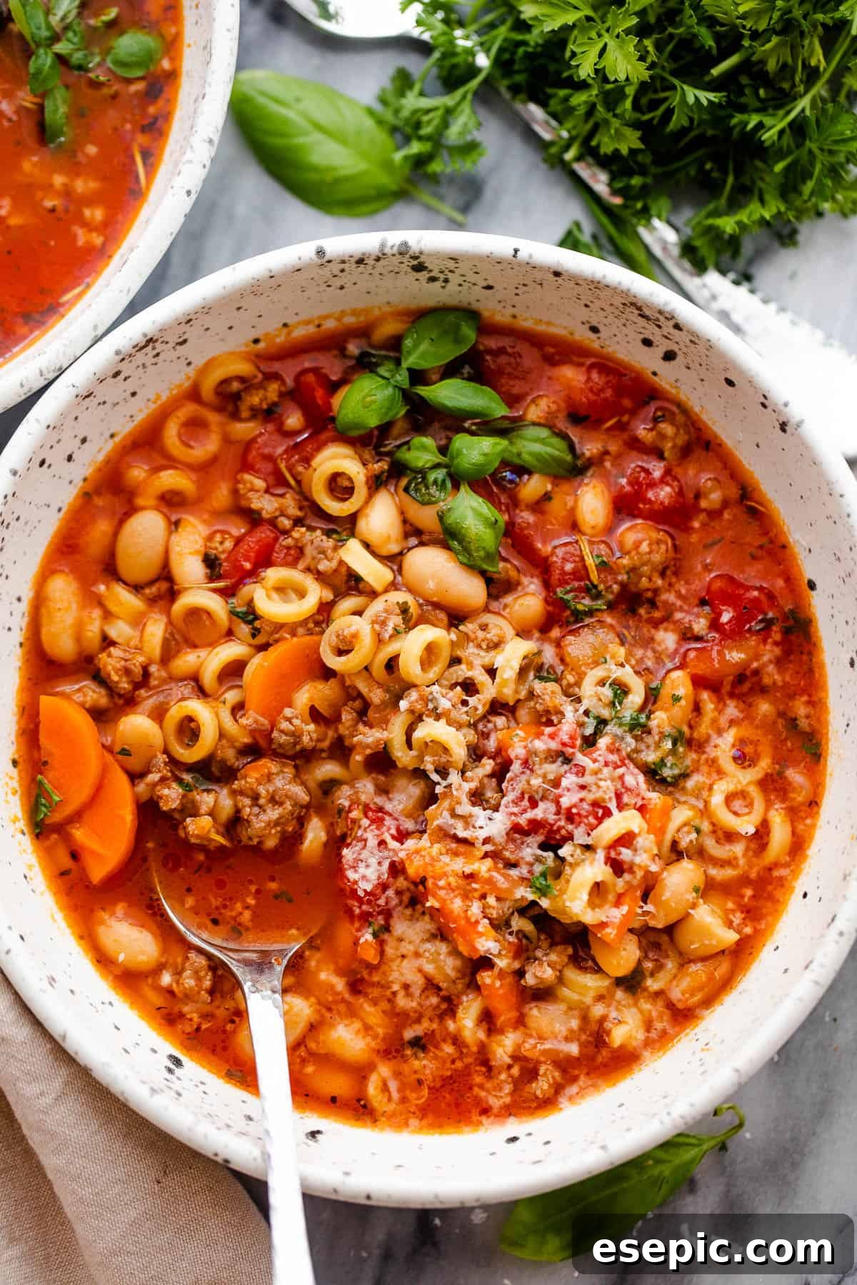 An overhead shot of a single serving of Pasta Fagioli soup in a white bowl with a spoon, garnished with Parmesan and parsley.
