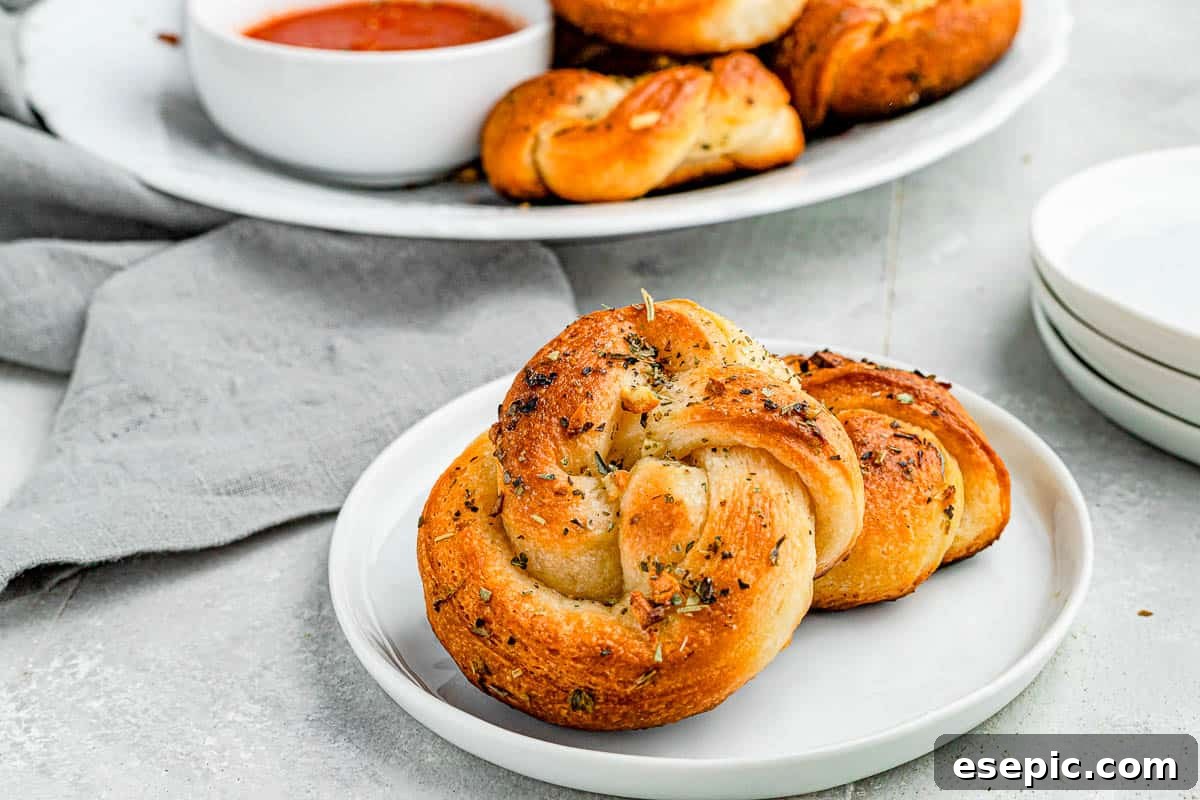 A wide shot of garlic knots piled onto a plate with marinara dipping sauce on the side.