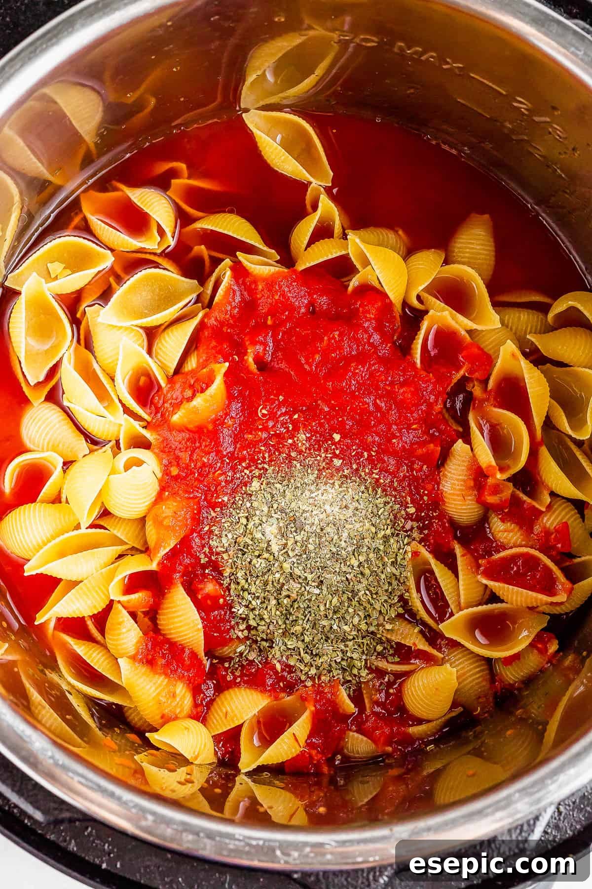 Instant Pot Hearty Beef and Shells 4 An overhead shot of an Instant Pot with crushed tomatoes, water, pasta, and seasonings inside.