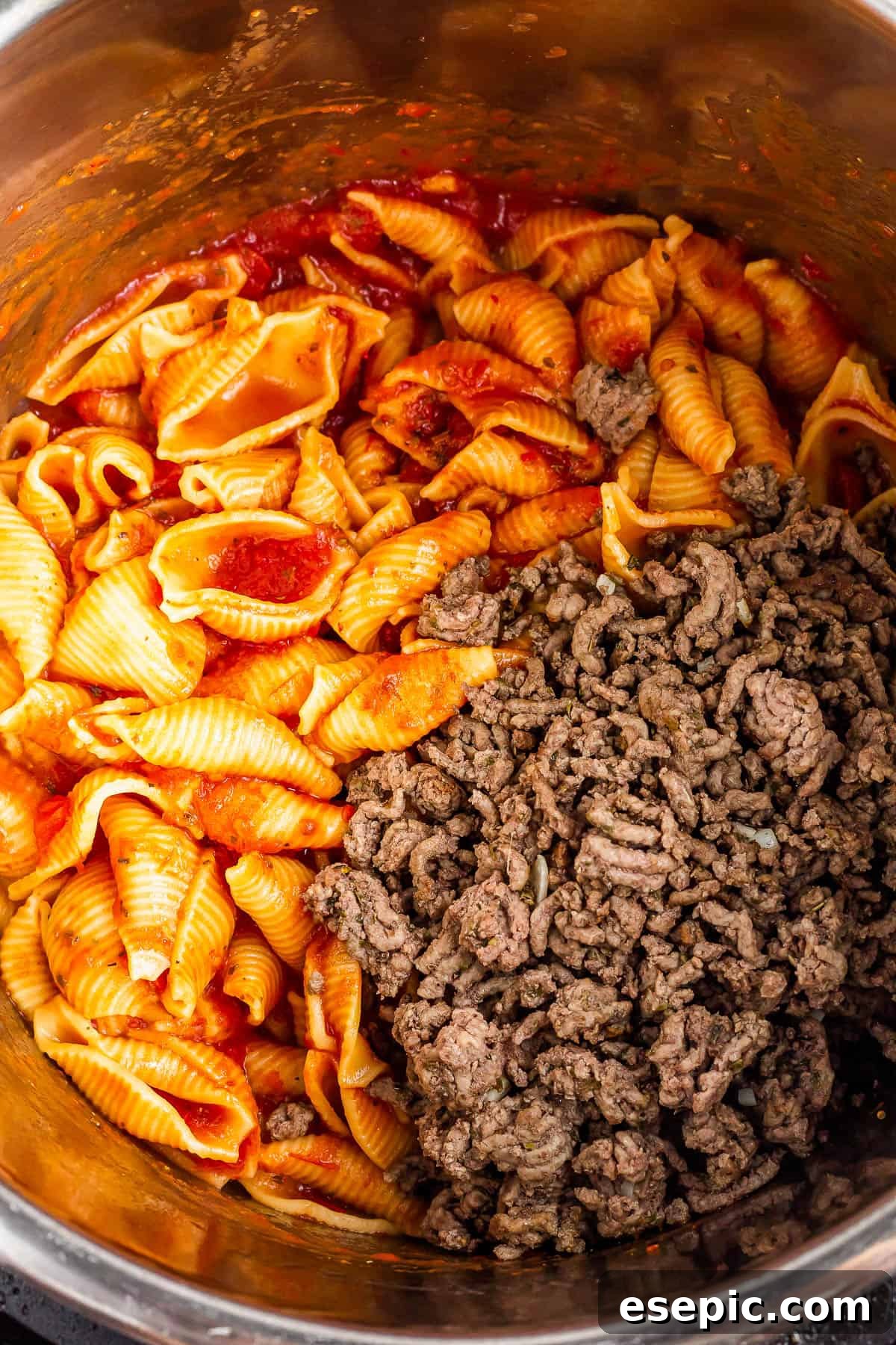 Instant Pot Hearty Beef and Shells 5 An overhead shot of an Instant Pot with cooked shells in sauce inside and a batch of browned ground beef added.