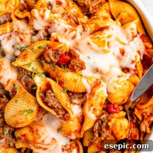 A serving dish filled with cooked pasta shells and ground beef in tomato sauce, topped with melted mozzarella.