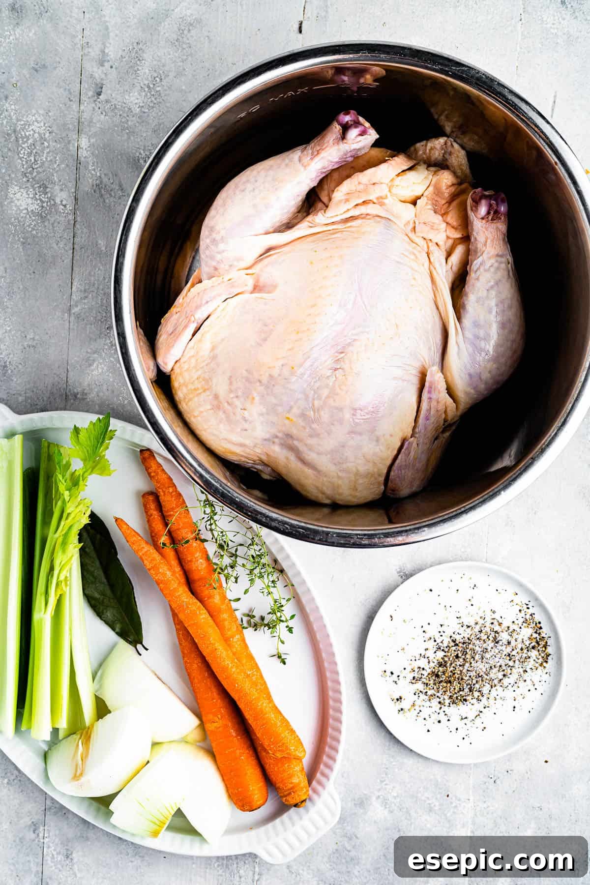 Clockwise from top: a plump whole chicken ready for cooking, a bowl of aromatic seasonings, and a tray of fresh, vibrant raw vegetables including carrots, onions, and celery, all essential ingredients for a rich chicken broth.
