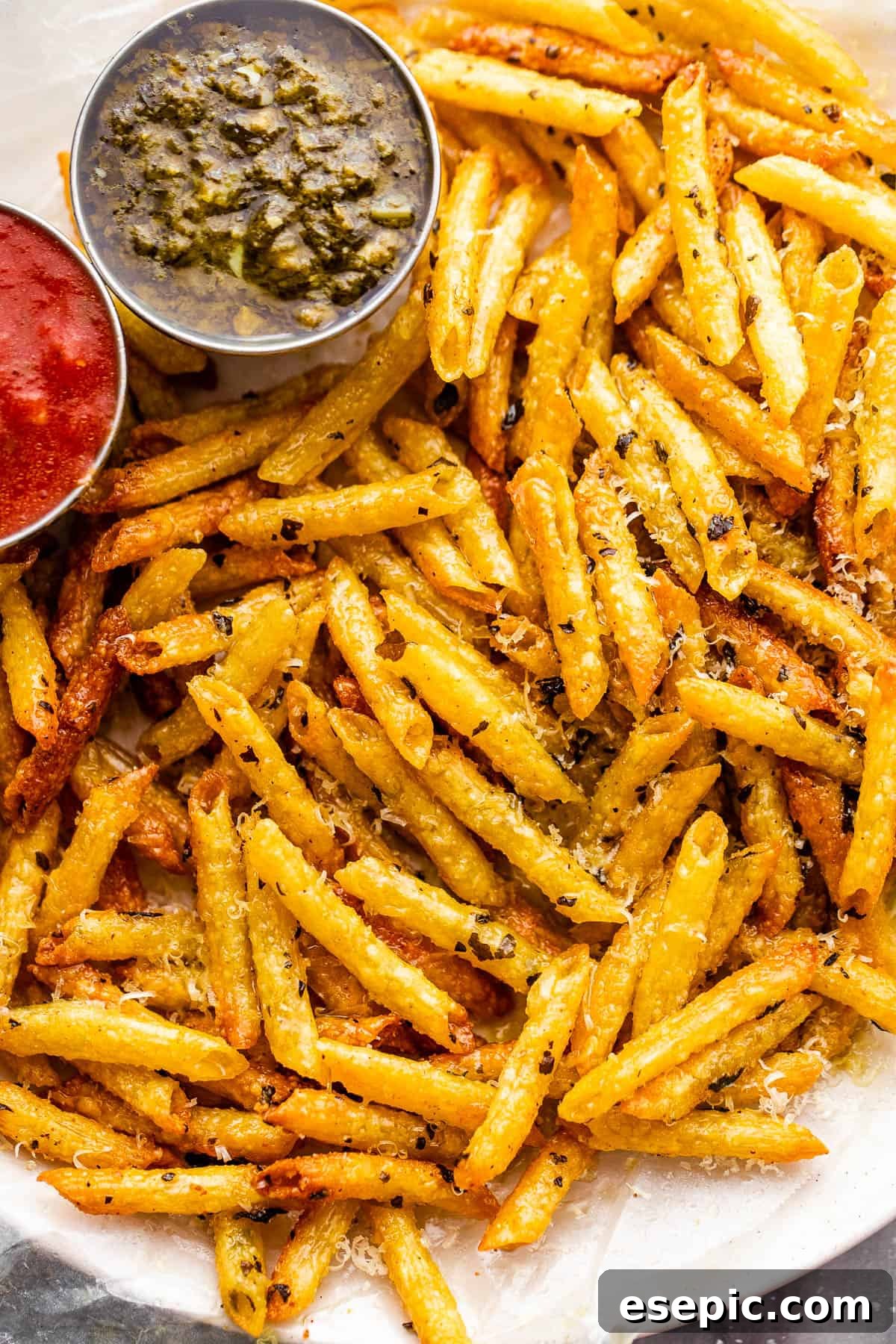 Crispy Pasta Chips Air Fry or Bake 2 Plate with golden-brown, baked pasta chips served alongside small bowls of vibrant basil pesto and rich marinara sauce, garnished with fresh basil leaves.