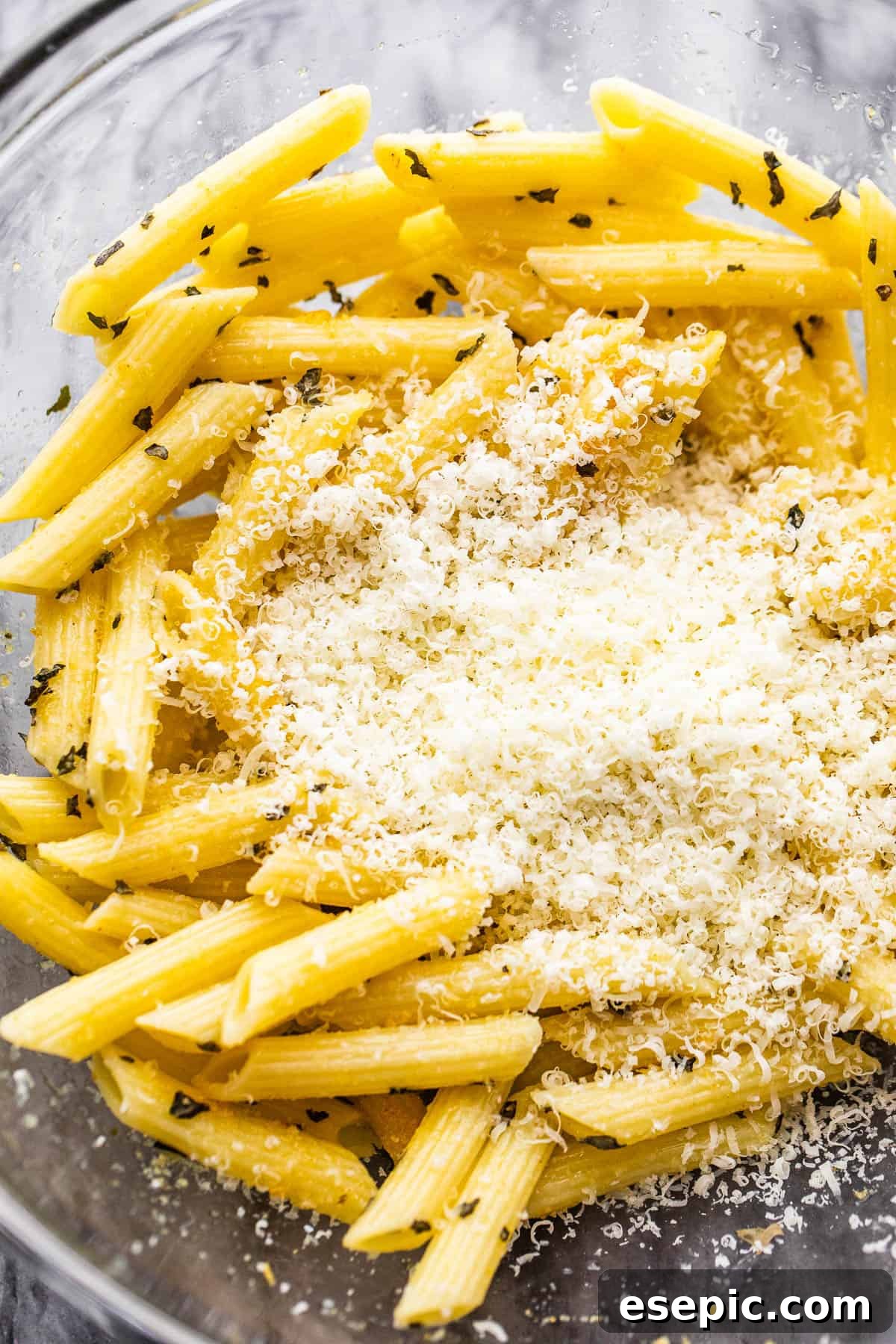 Crispy Pasta Chips Air Fry or Bake 4 A bowl of boiled pasta ready for seasoning, with a small mound of grated Parmesan cheese in the center, highlighting key ingredients.