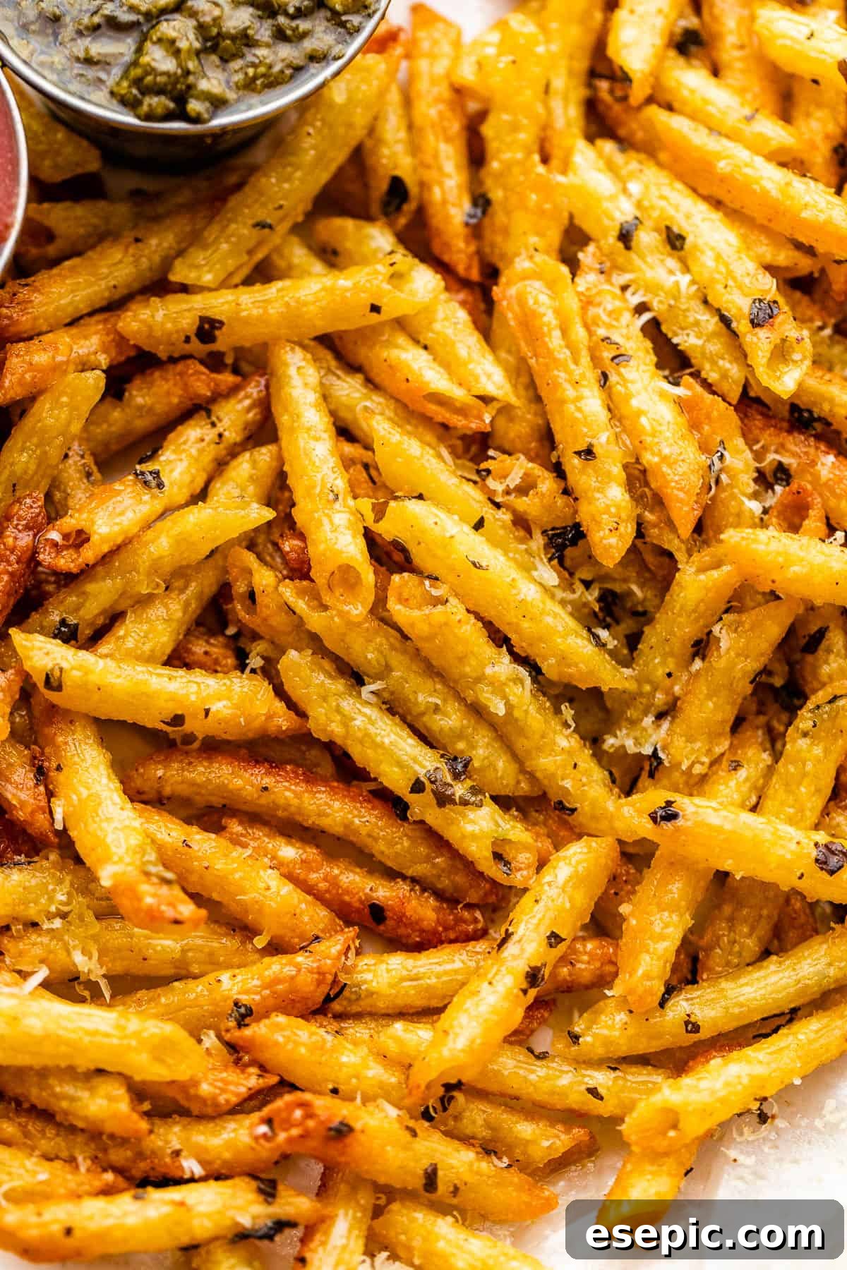 Crispy Pasta Chips Air Fry or Bake 6 A close-up of a plate piled high with golden-brown, crispy pasta chips, accompanied by a small bowl of fresh basil pesto for dipping.