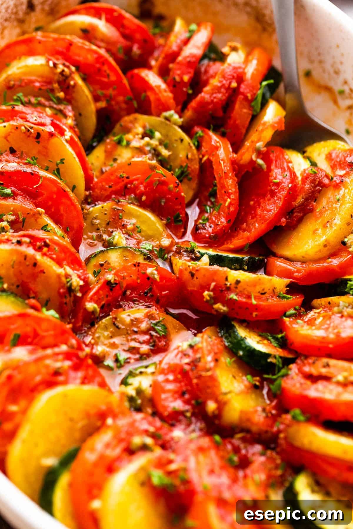 close up shot of zucchini slices, tomato slices, and potato slices arranged accordion style in a baking dish.
