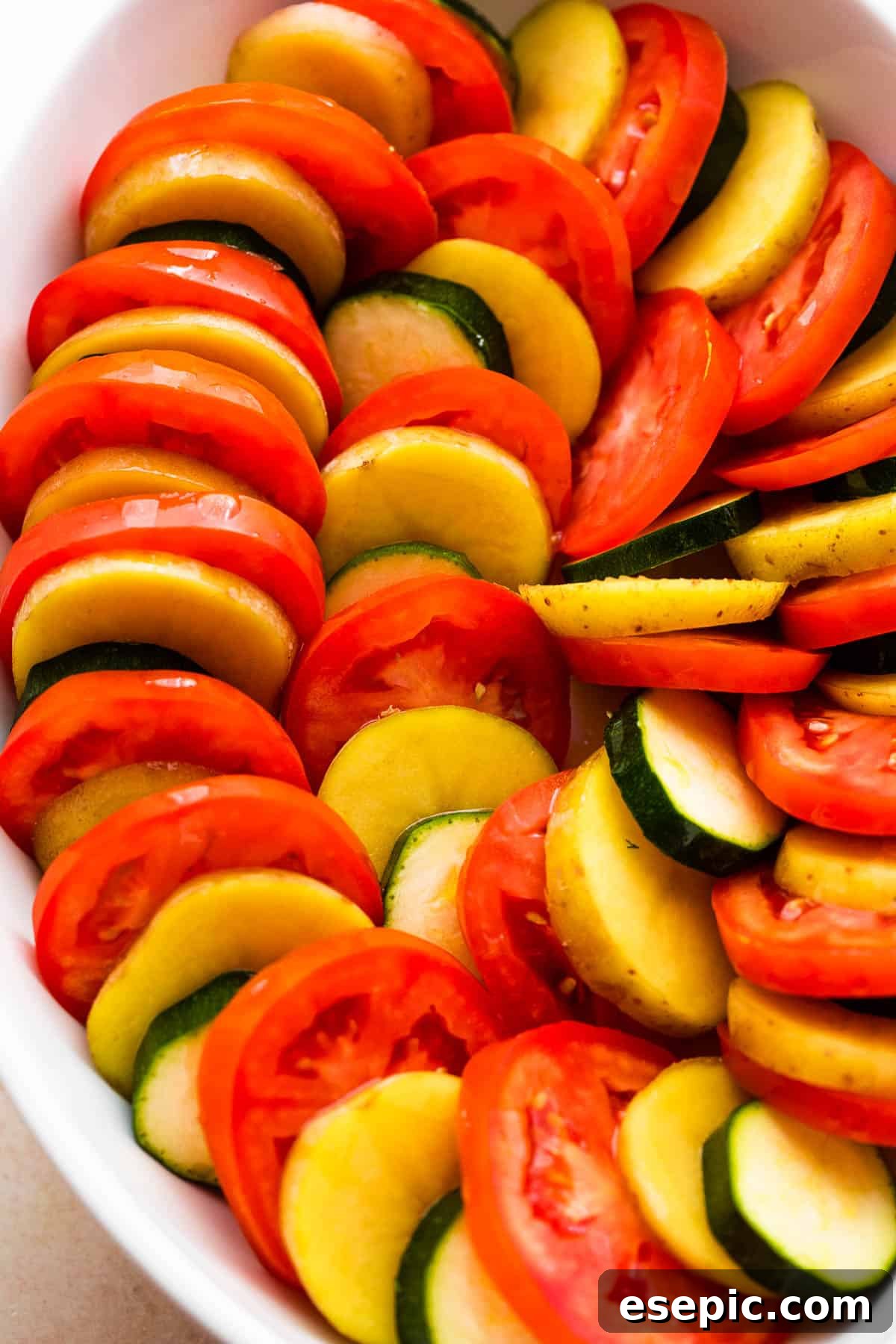 overhead shot of zucchini, tomato, and potato slices arranged accordion style in a baking dish.