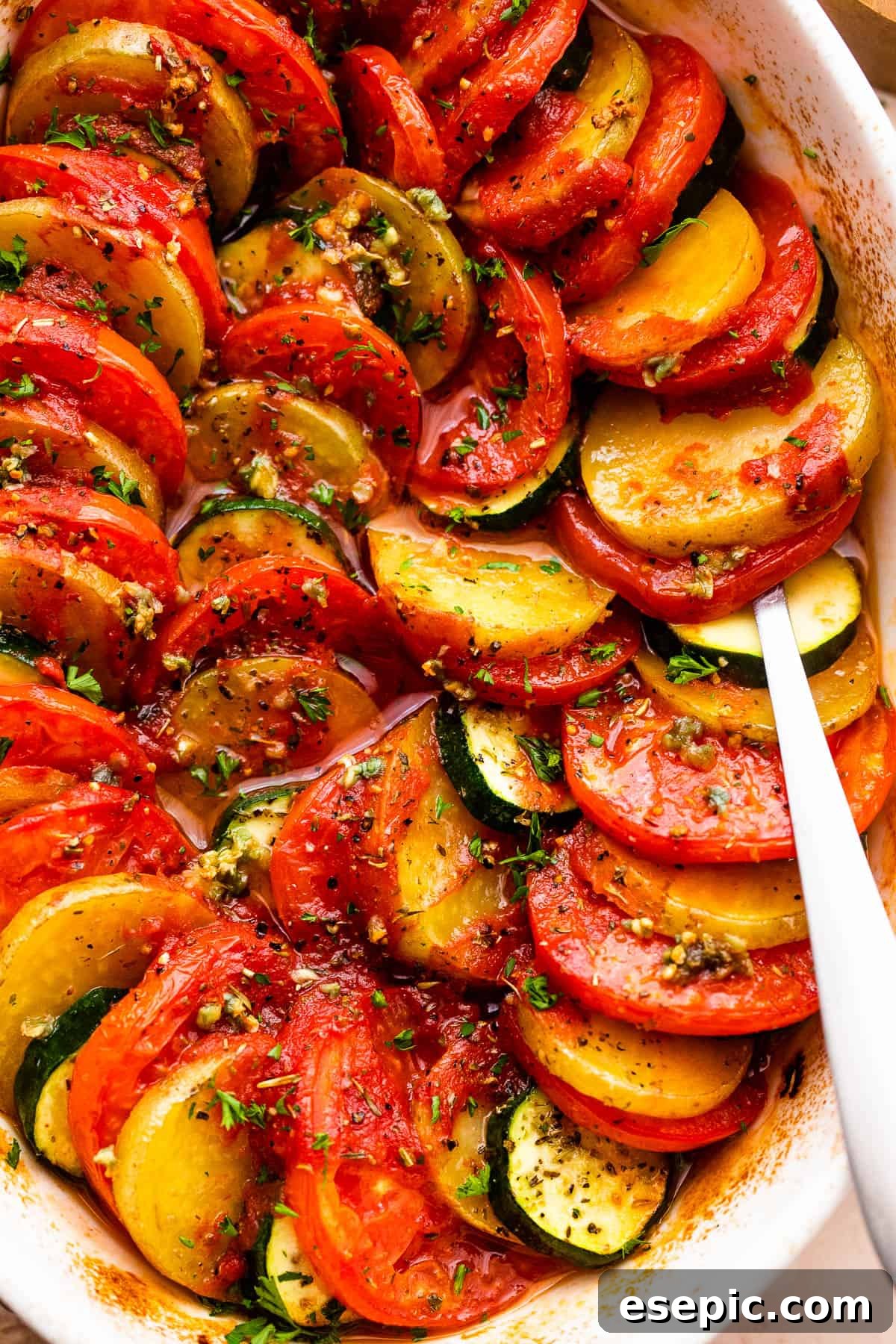 close up shot of zucchini slices, tomato slices, and potato slices arranged accordion style in a baking dish.