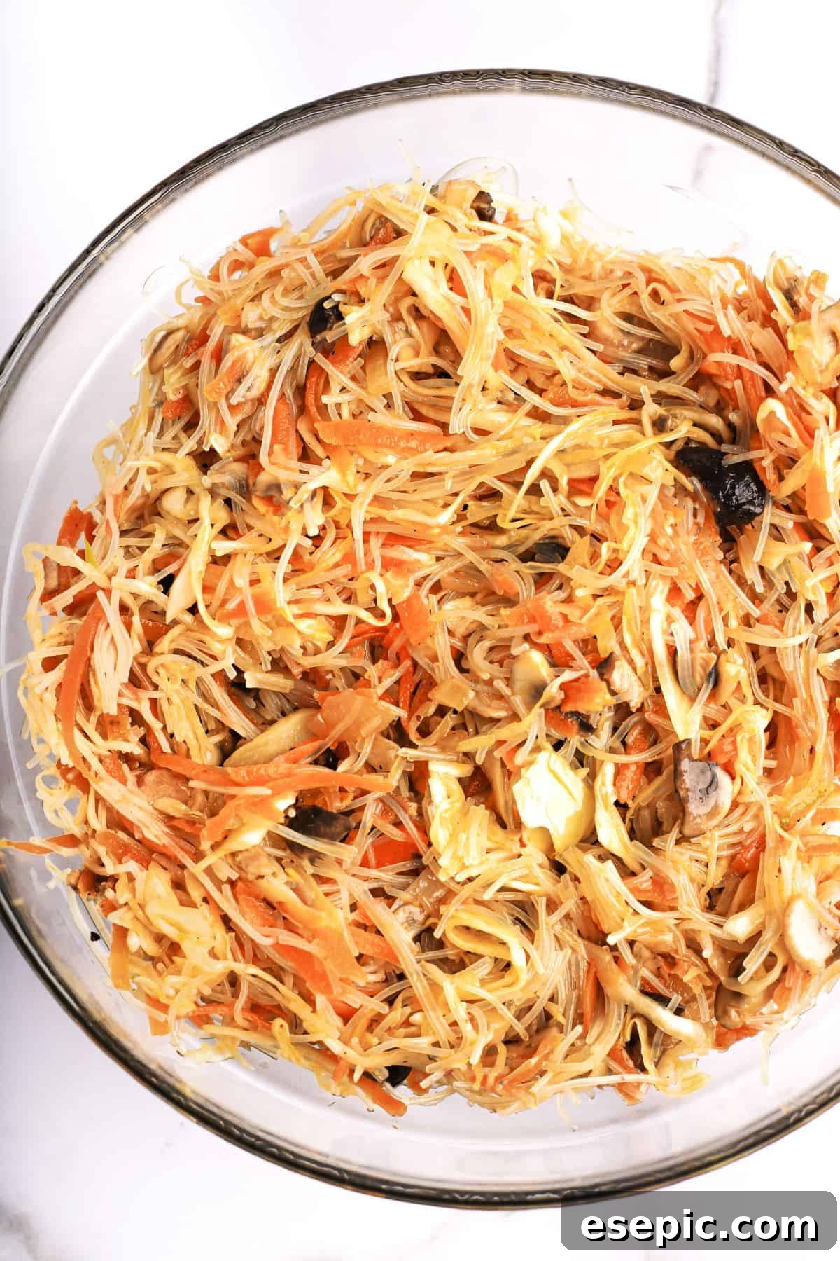 A vibrant bowl of spring roll filling, featuring an appetizing mix of rice vermicelli noodles, shredded carrots, sliced shiitake mushrooms, and other colorful vegetables, ready for wrapping.
